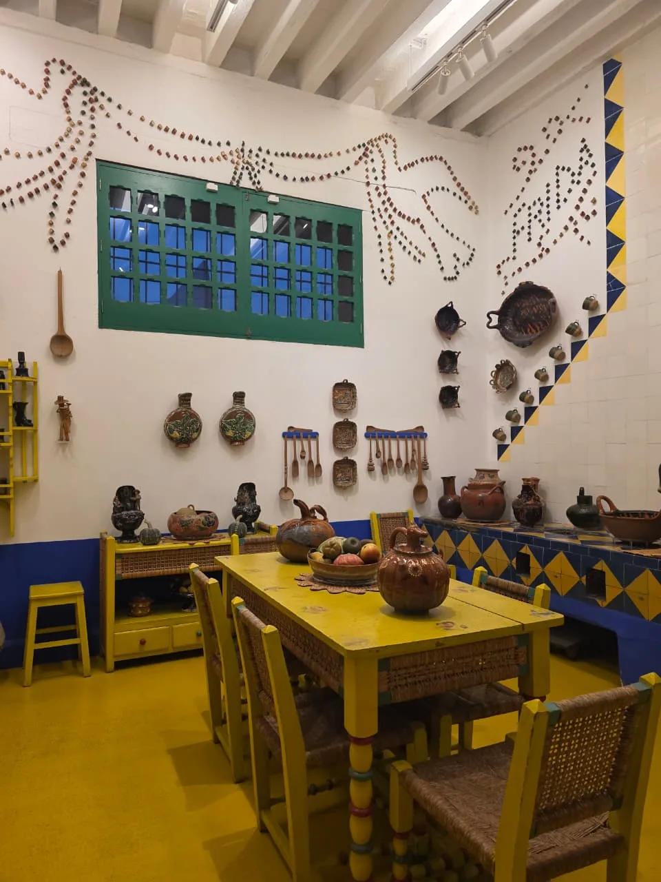 ครัวภายใน Casa Azul ผนังขาวประดับหม้อดินเผาขนาดเล็ก โต๊ะและพื้นสีเหลือง ภาพถ่ายเดือนมีนาคม 2026