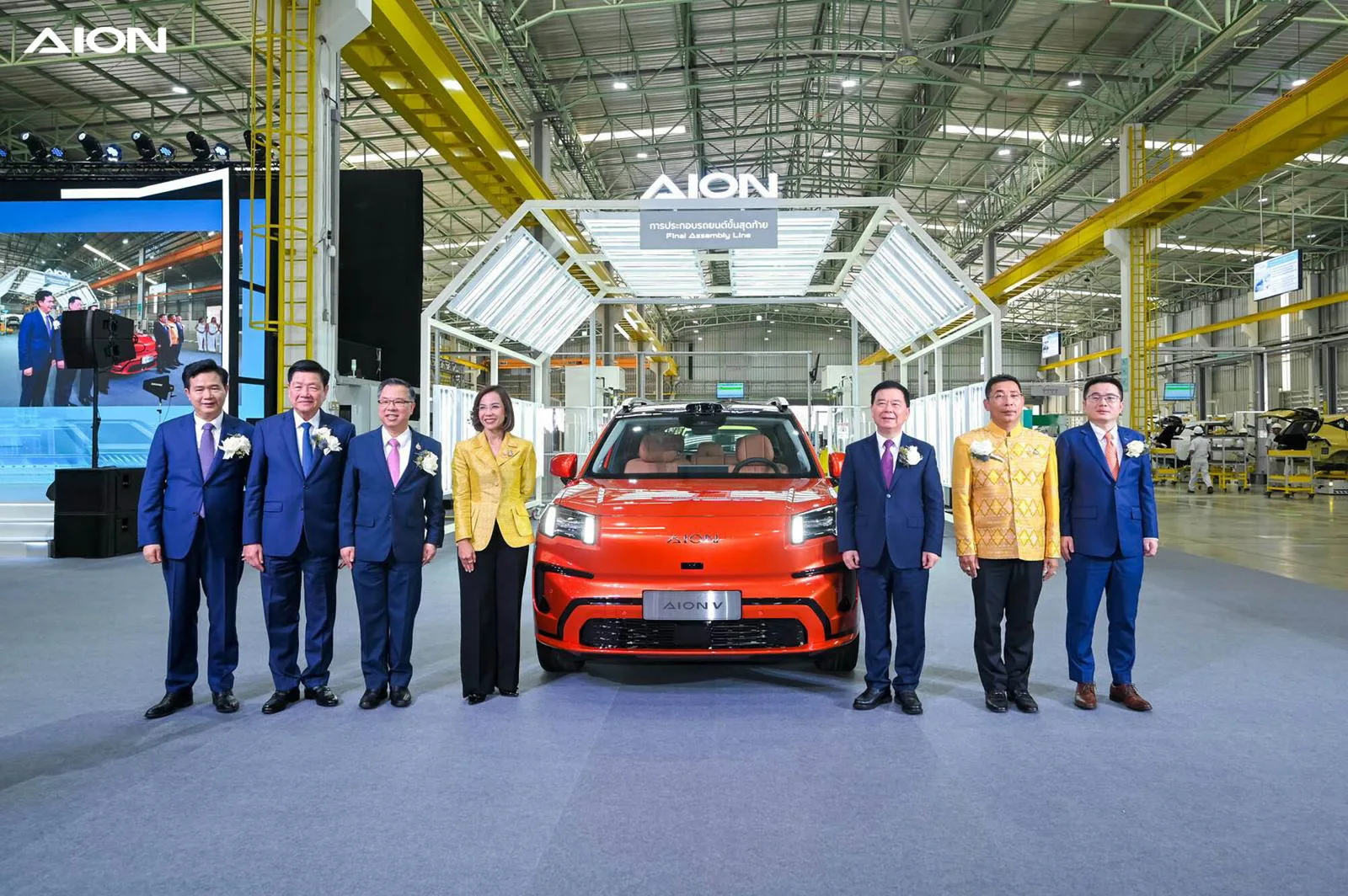 AION V สีส้มจอดหน้าป้ายการประกอบรถยนต์ขั้นสุดท้าย Final Assembly Line ในโรงงาน GAC AION ระยอง โดยมีผู้บริหารยืนสองข้าง