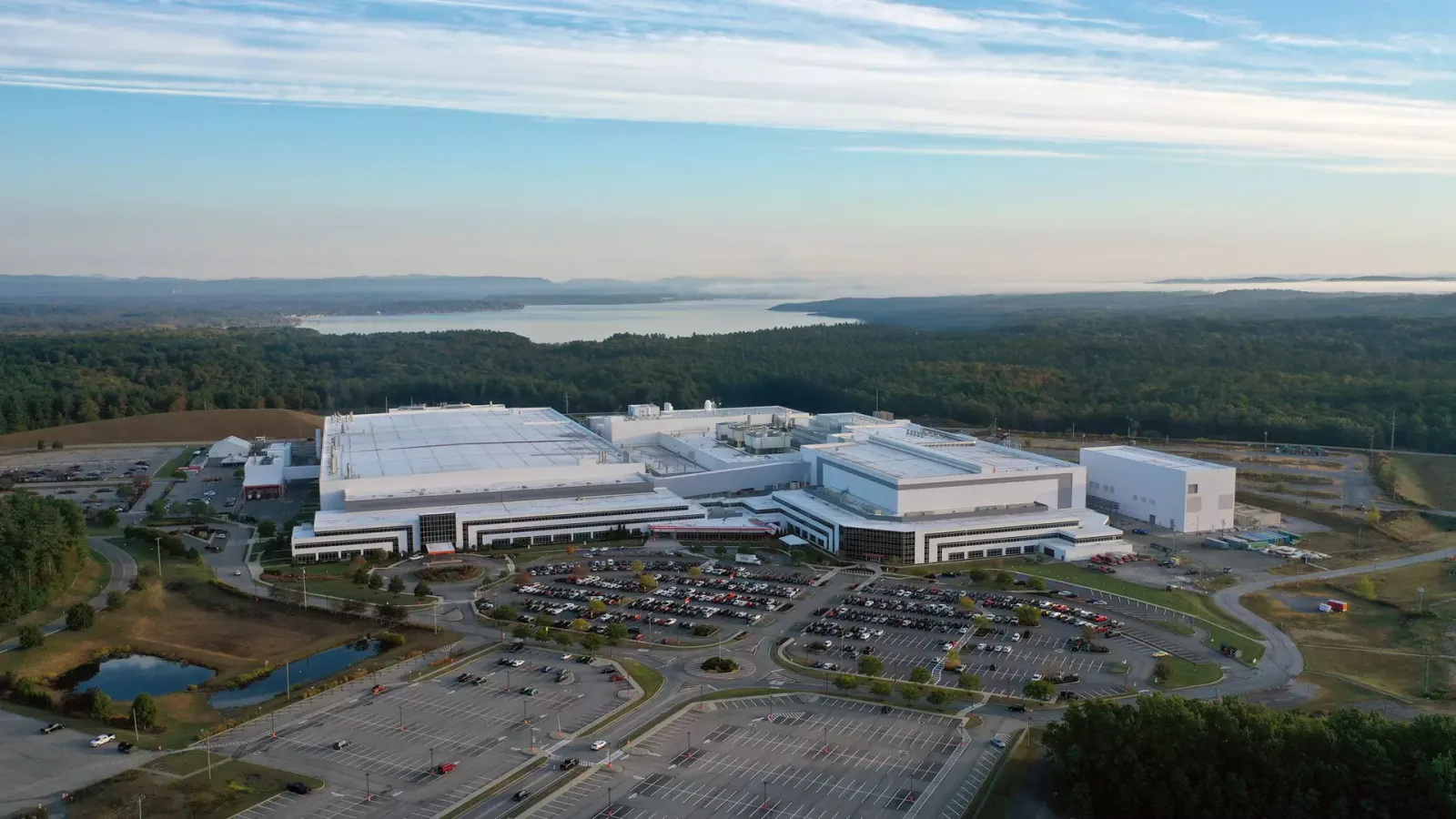 ภาพมุมสูงโรงงานผลิตชิปของ GlobalFoundries ที่มอลตา รัฐนิวยอร์ก อาคารสีขาวขนาดใหญ่ริมป่าและทะเลสาบ
