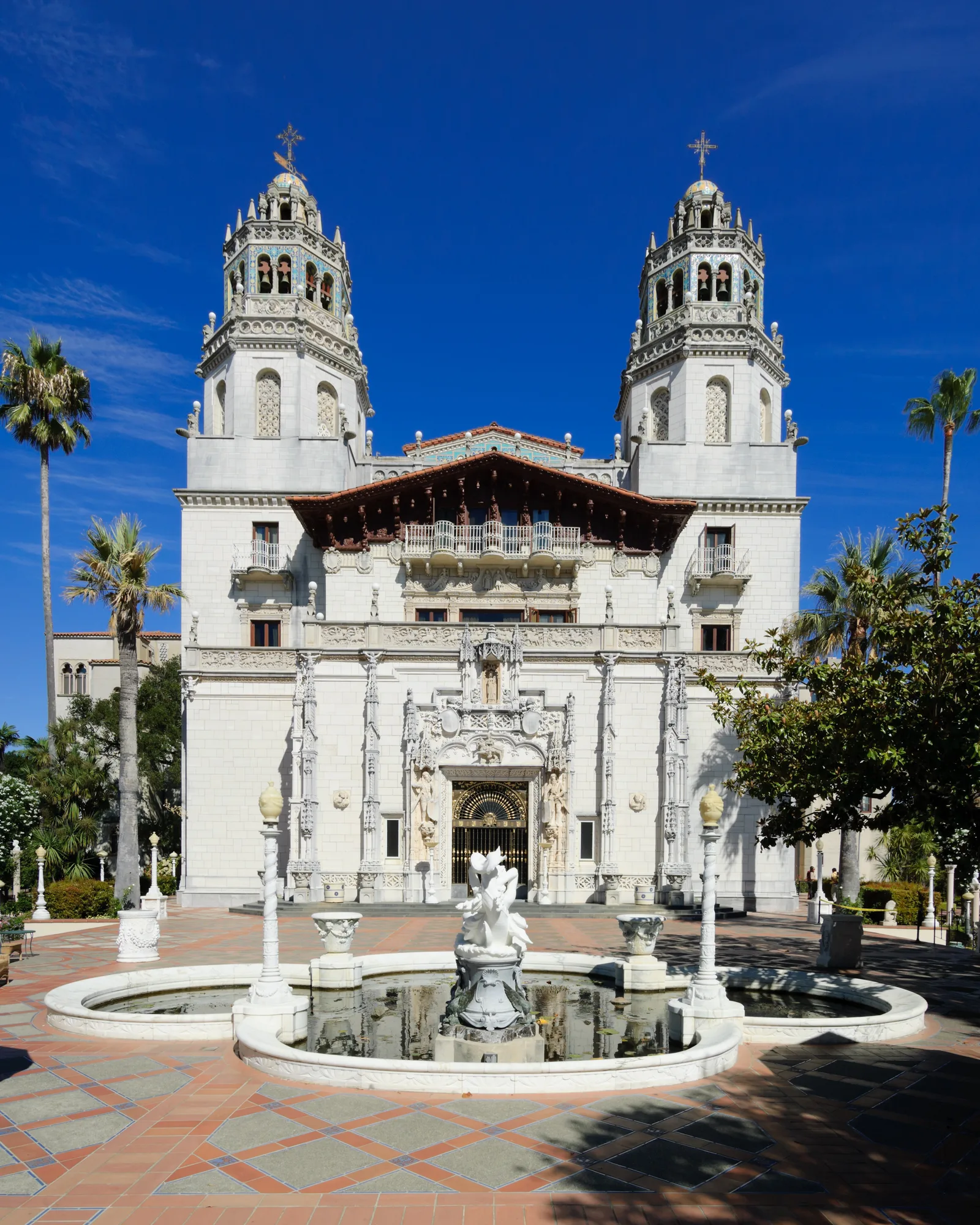 ด้านหน้า Casa Grande บ้านหลักของ Hearst Castle มีหอคอยคู่ บ่อน้ำพุกลางลาน และต้นปาล์มสองข้าง