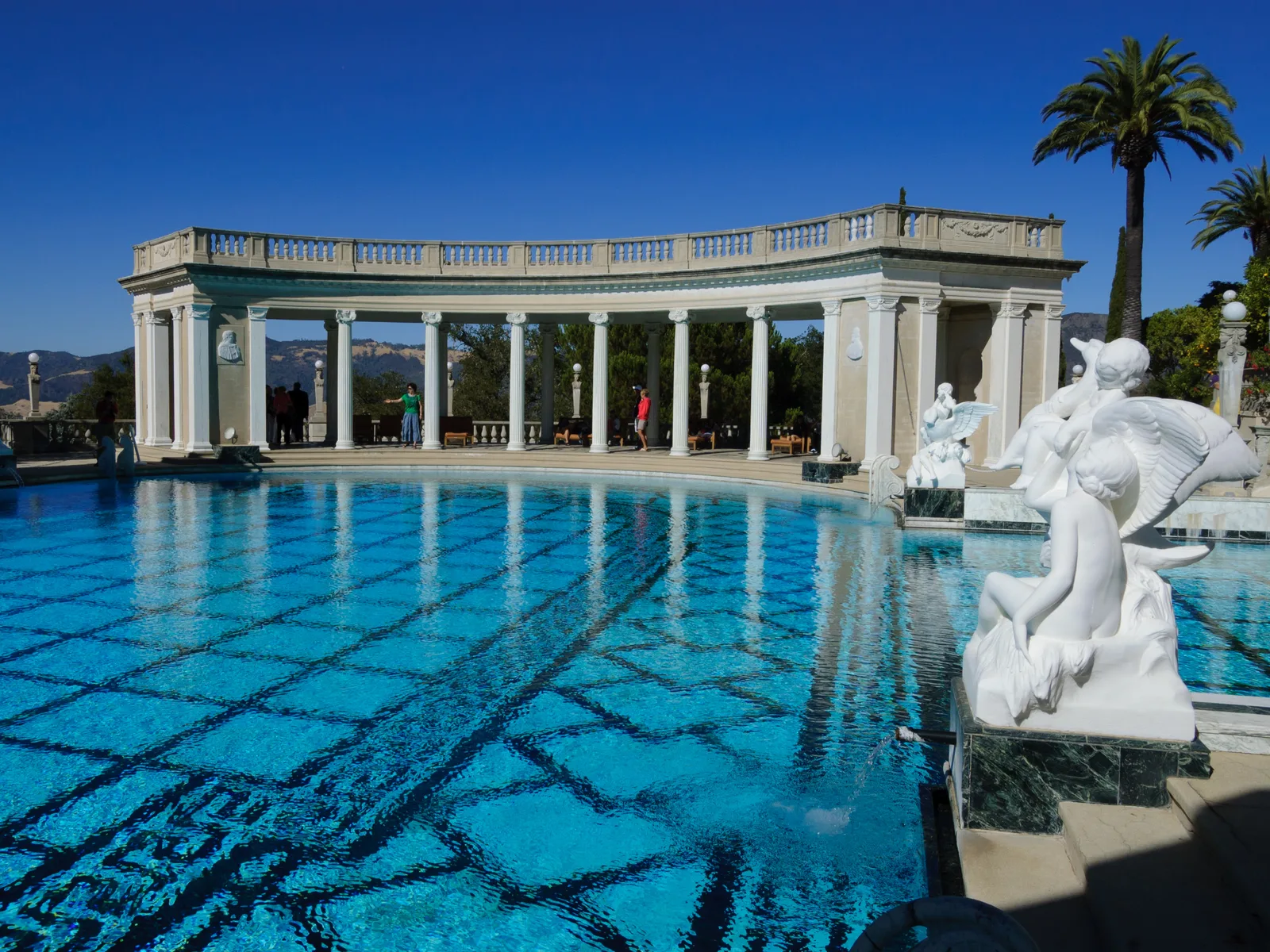 Neptune Pool ของ Hearst Castle น้ำสีฟ้าใส แนวเสาหินอ่อนโค้งรอบสระ และรูปปั้นสีขาวริมขอบสระ