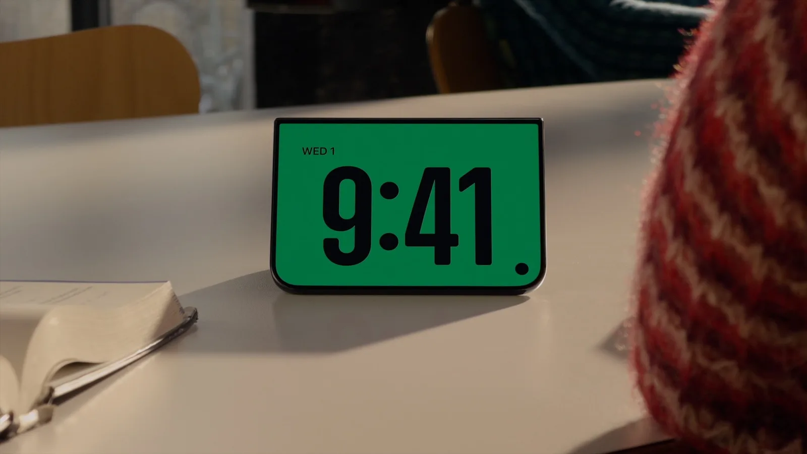 iPhone Duo ตั้งอยู่บนโต๊ะในโหมดสแตนด์บาย แสดงเวลา 9:41 ตัวใหญ่บนพื้นสีเขียว