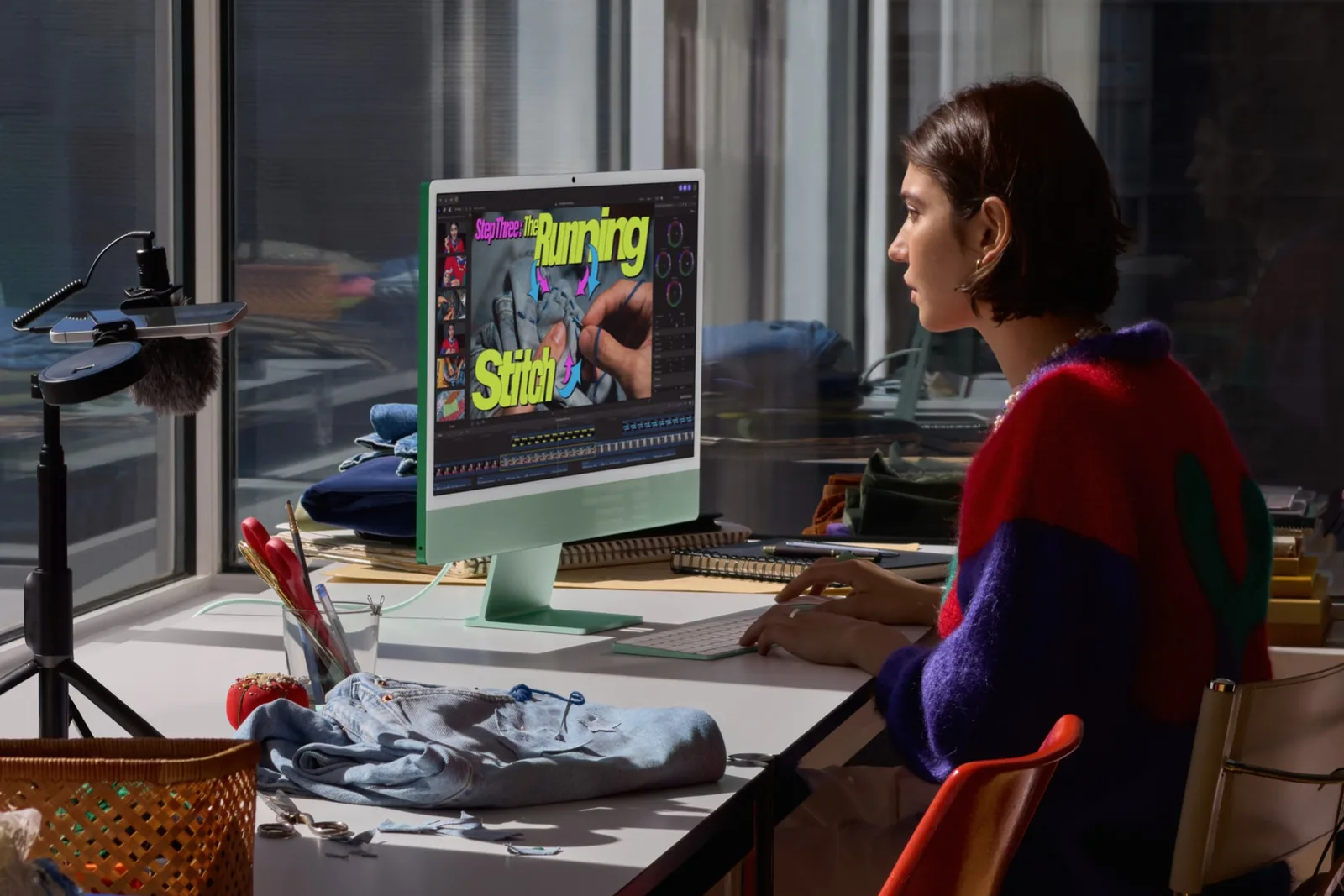 ผู้ใช้นั่งตัดต่อวิดีโอบน iMac สีเขียวที่โต๊ะริมหน้าต่าง