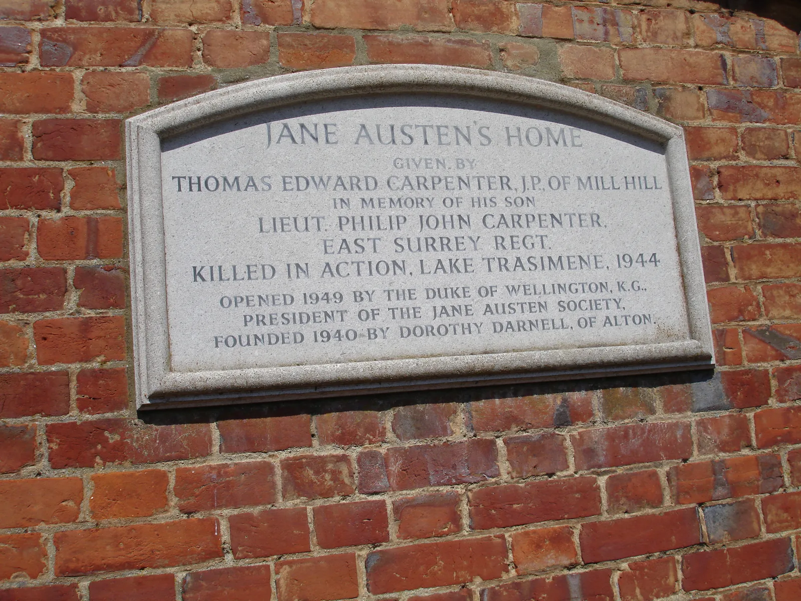 แผ่นจารึกบนผนังบ้านของ Jane Austen ระบุชื่อ Thomas Edward Carpenter ผู้มอบบ้านเพื่อรำลึกถึงลูกชาย และปีที่เปิดบ้าน 1949 ภาพถ่ายเดือนสิงหาคม 2006