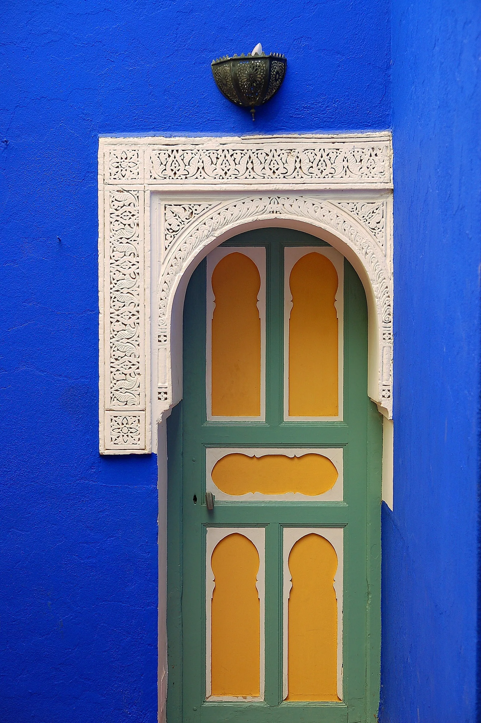 ประตูไม้ทรงโค้งในกรอบปูนปั้นสีขาวบนผนังสีน้ำเงินของ Jardin Majorelle ภาพถ่ายเมื่อ 10 กรกฎาคม 2006