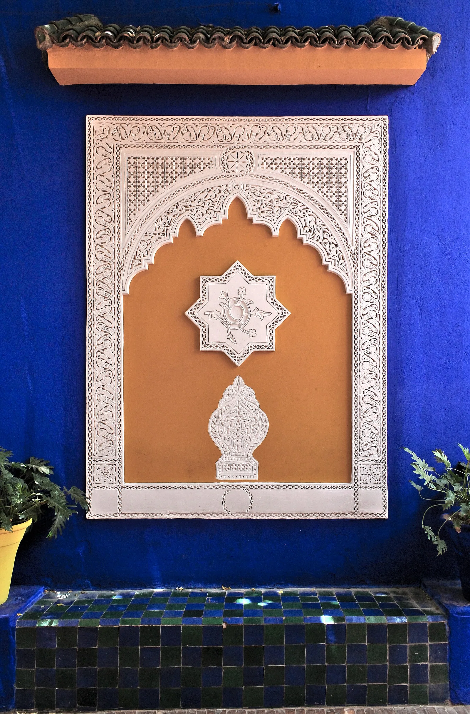 ซุ้มปูนปั้นบนผนังสีน้ำเงินเหนือม้านั่งปูกระเบื้องใน Jardin Majorelle ภาพถ่ายเมื่อ 14 กรกฎาคม 2014