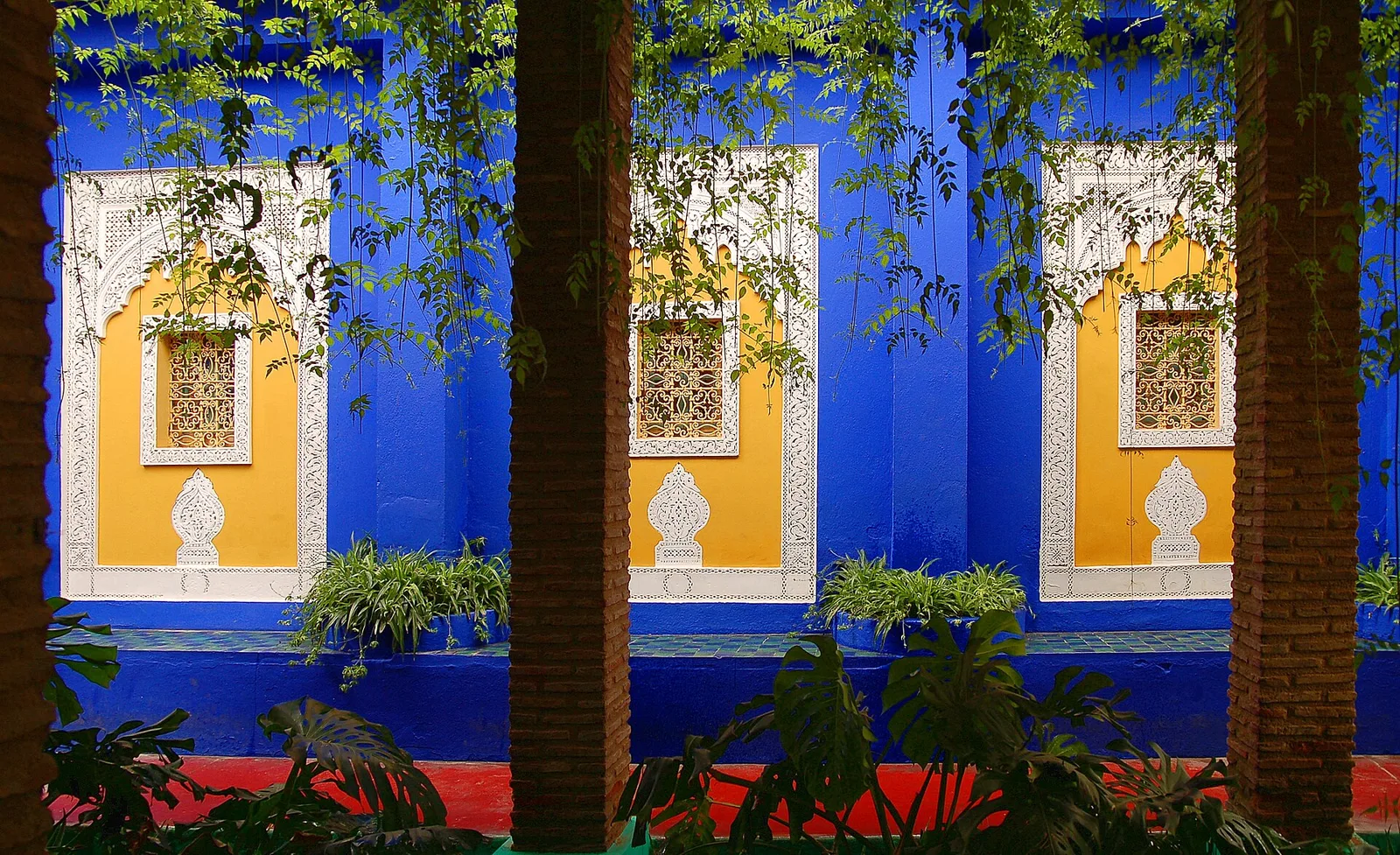 ซุ้มปูนปั้นสีขาวพื้นเหลืองสามซุ้มบนผนังสีน้ำเงินใน Jardin Majorelle ภาพถ่ายเมื่อ 10 กรกฎาคม 2006