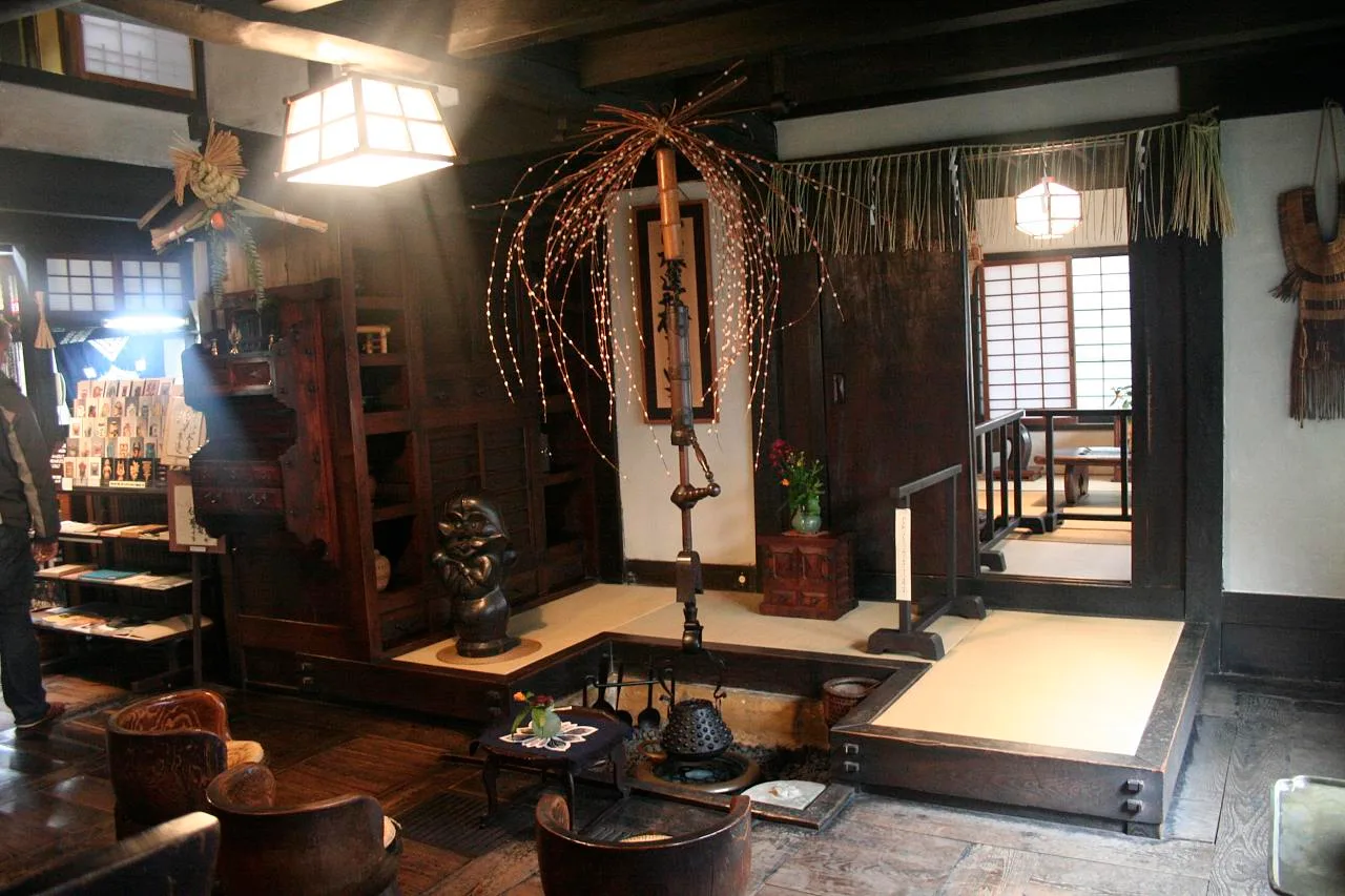 ห้องในบ้านของ Kawai Kanjiro ที่เกียวโต มีเตาไฟฝังพื้น เก้าอี้ไม้ โคมไฟ และกิ่งไม้ประดับ ภาพถ่ายเดือนมกราคม 2008