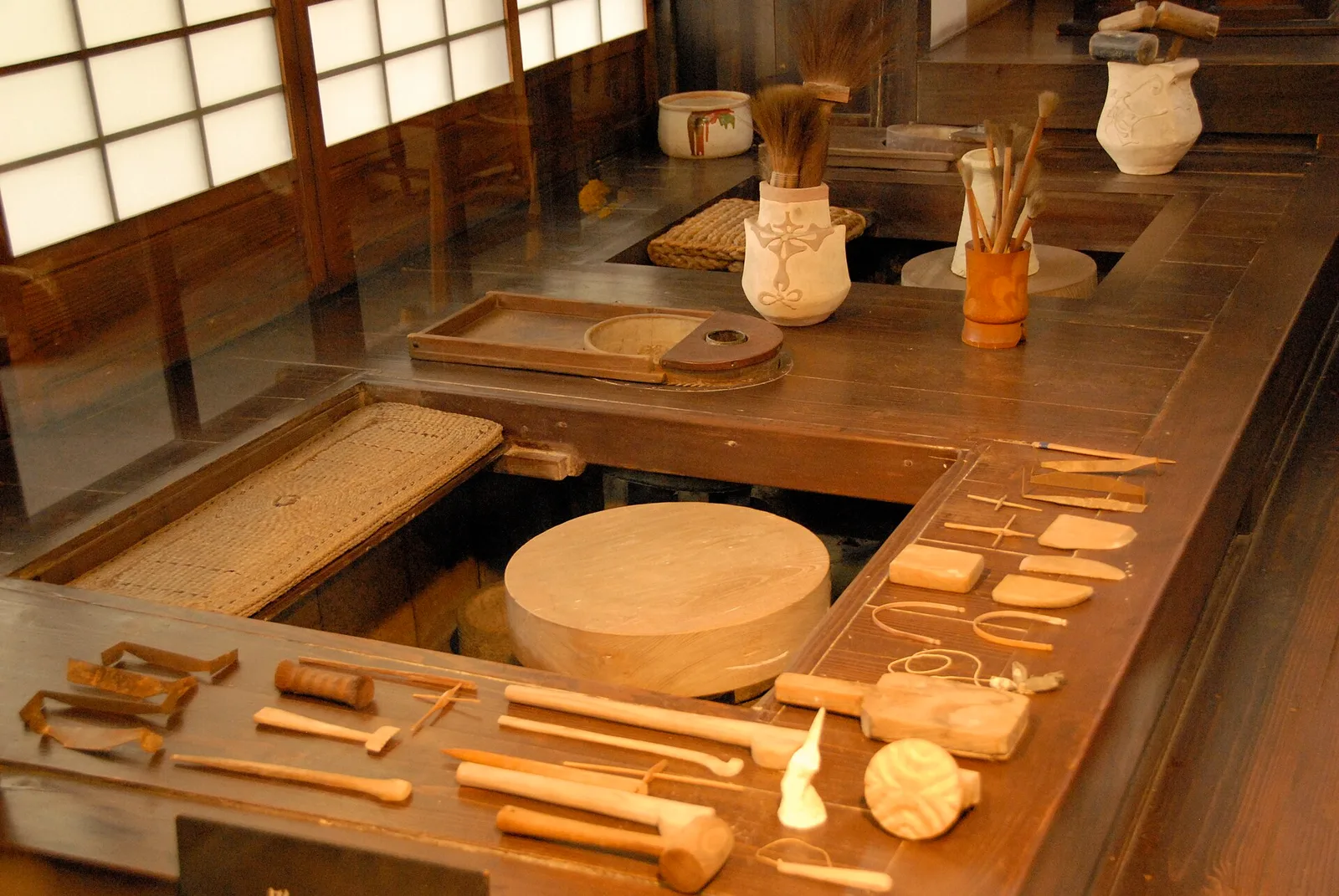 มุมทำงานในบ้านของ Kawai Kanjiro ที่เกียวโต มีแป้นหมุน เครื่องมือปั้น และภาชนะวางเรียงริมหน้าต่าง ภาพถ่ายเดือนพฤศจิกายน 2009