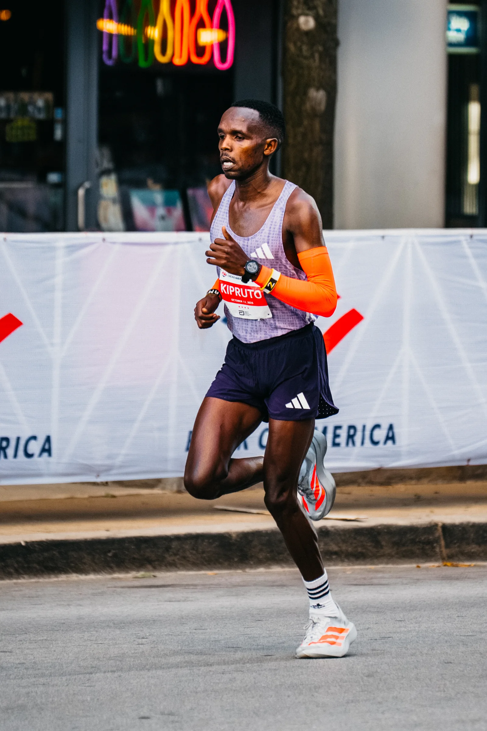 Amos Kipruto นักวิ่งเคนยาในเสื้อกล้าม กางเกงขาสั้น ปลอกแขน นาฬิกา และรองเท้าวิ่งมาราธอน ติดป้ายชื่อ KIPRUTO ช่วงไมล์ที่ 25 ของ Chicago Marathon 2025