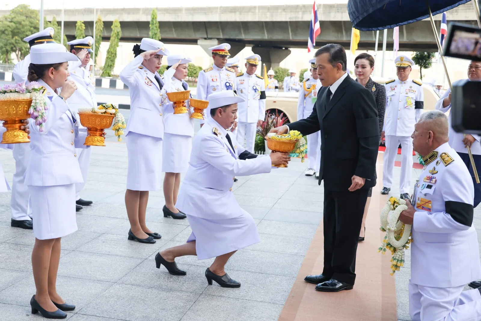 แถวข้าราชการในเครื่องแบบสีขาว เฝ้าทูลละอองธุลีพระบาทรับเสด็จ ด้านหน้าอาคาร