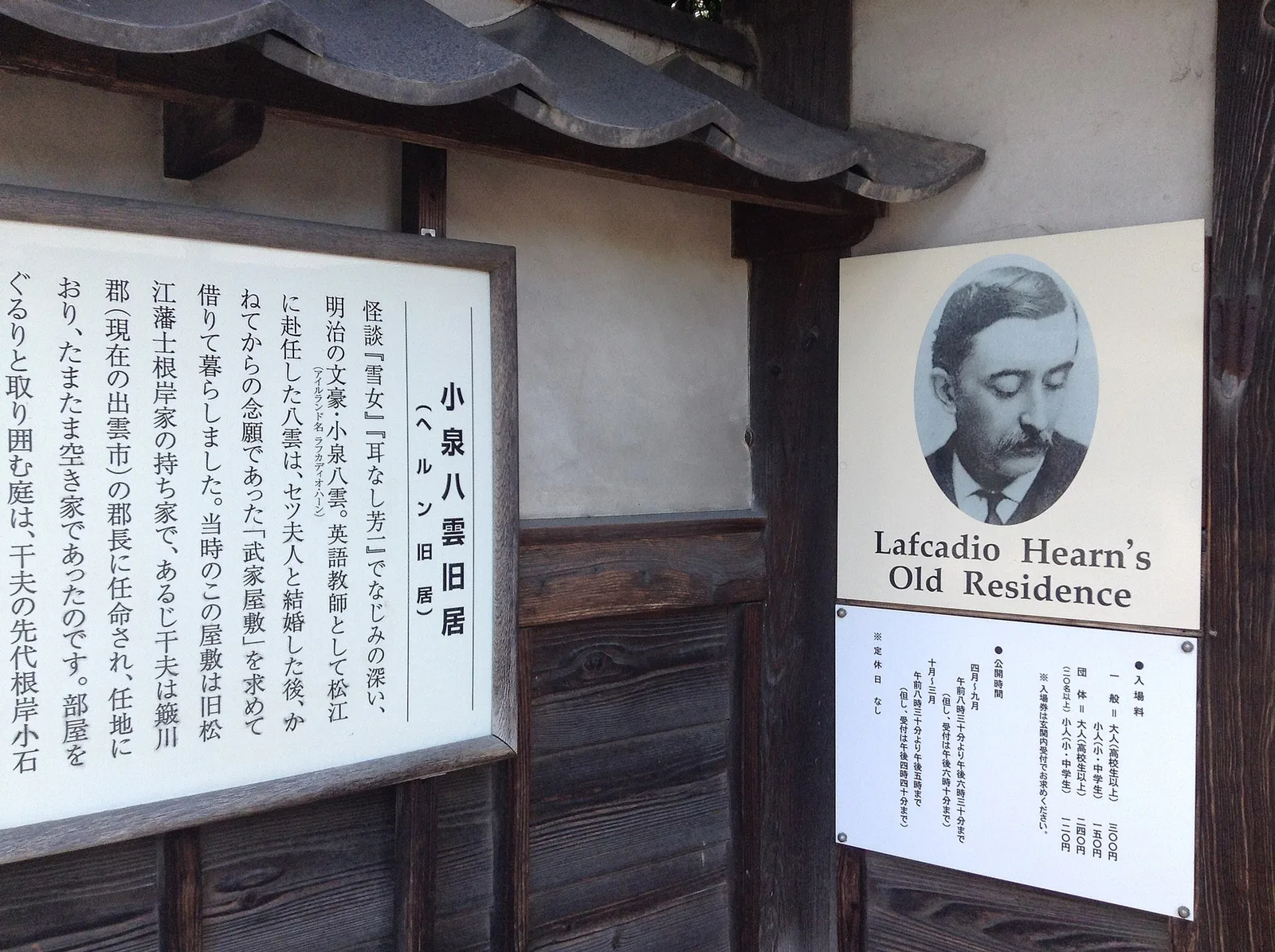ป้ายข้อมูลภาษาญี่ปุ่นและอังกฤษหน้าบ้านพักเดิมของ Lafcadio Hearn พร้อมภาพเหมือนของเขา ภาพถ่ายเดือนกันยายน 2014