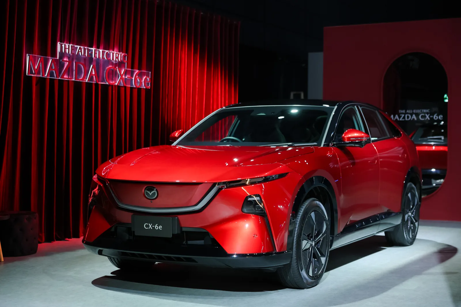 Mazda CX-6e สีแดงตัดดำ จอดหน้าม่านสีแดงในโซนจัดแสดง