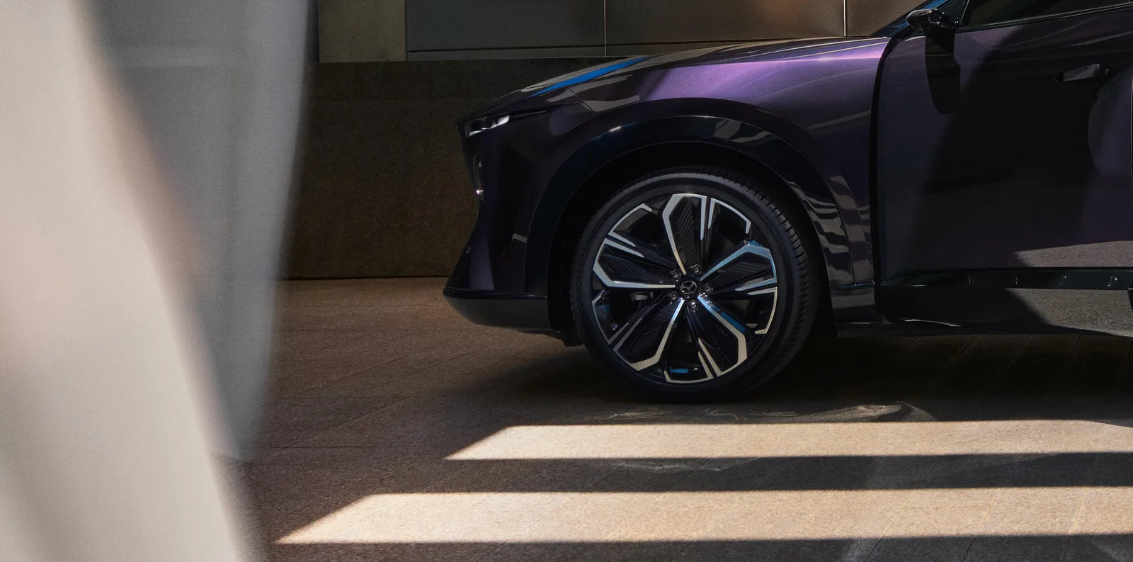 ล้ออัลลอยและซุ้มล้อหน้าของ Mazda CX-6e สีม่วง จอดในอาคาร ภาพจากหน้ารุ่นรถของ Mazda ประเทศไทย