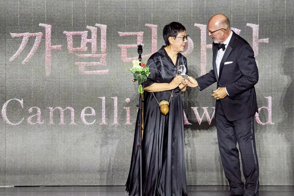 Ann Hui รับถ้วยรางวัล Camellia Award จาก Klaus Oldeget บนเวทีพิธีเปิด BIFF ครั้งที่ 31 หน้าจอด้านหลังมีชื่อรางวัลภาษาเกาหลีและอังกฤษ