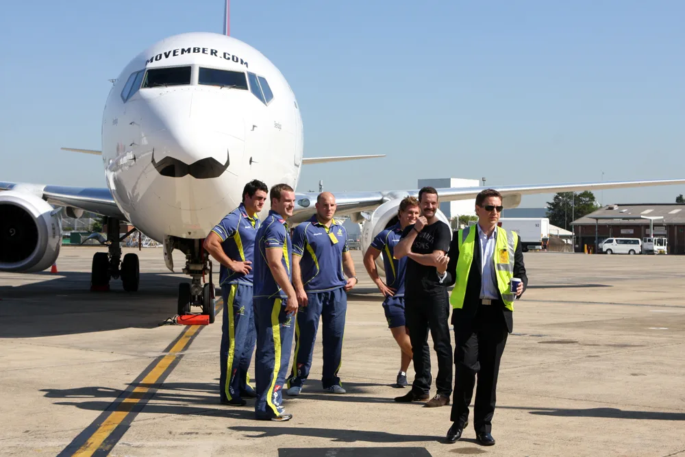 เครื่องบินโบอิ้ง 737-800 ทาสีหนวดขนาดใหญ่ มีข้อความ MOVEMBER.COM ที่จมูกเครื่อง