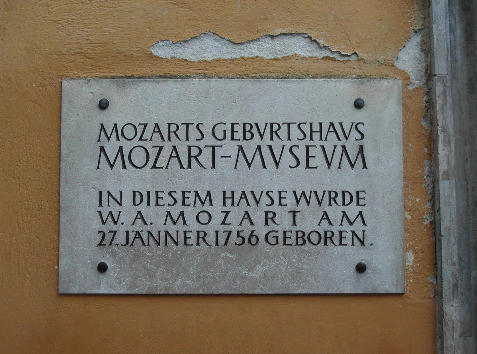 แผ่นจารึกหน้าบ้านโมสาร์ทหลังแรกเขียนว่า Mozarts Geburtshaus Mozart-Museum In diesem Hause wurde W. A. Mozart am 27. Jänner 1756 geboren ภาพถ่ายปี 2005