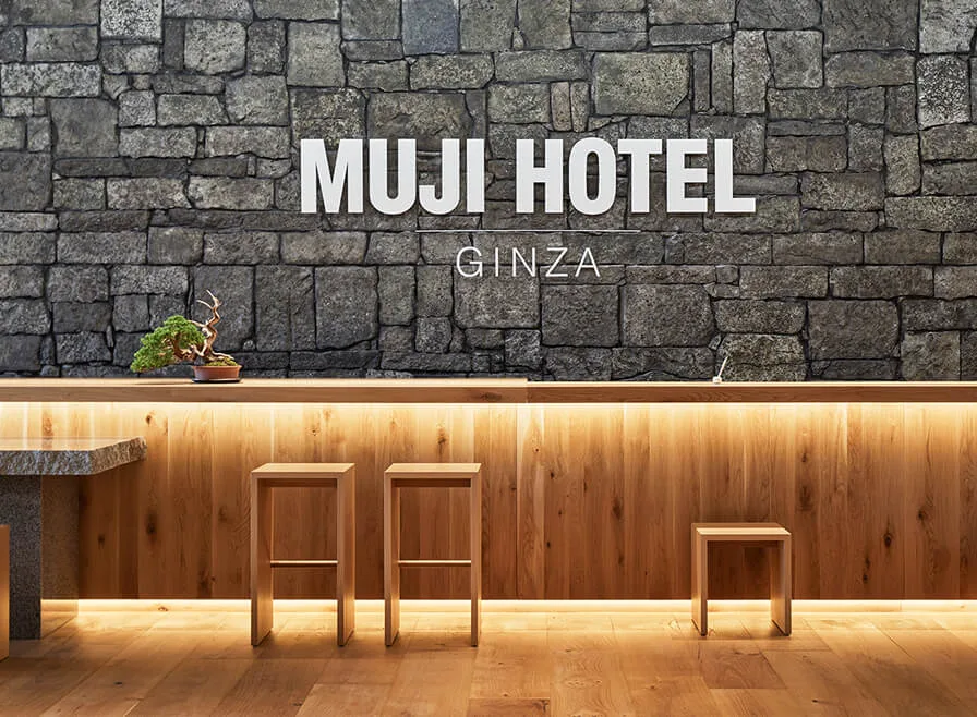 ผนังหินและเคาน์เตอร์ไม้ มีตัวอักษร MUJI HOTEL GINZA ภายในโรงแรมของแบรนด์ MUJI ในโตเกียว