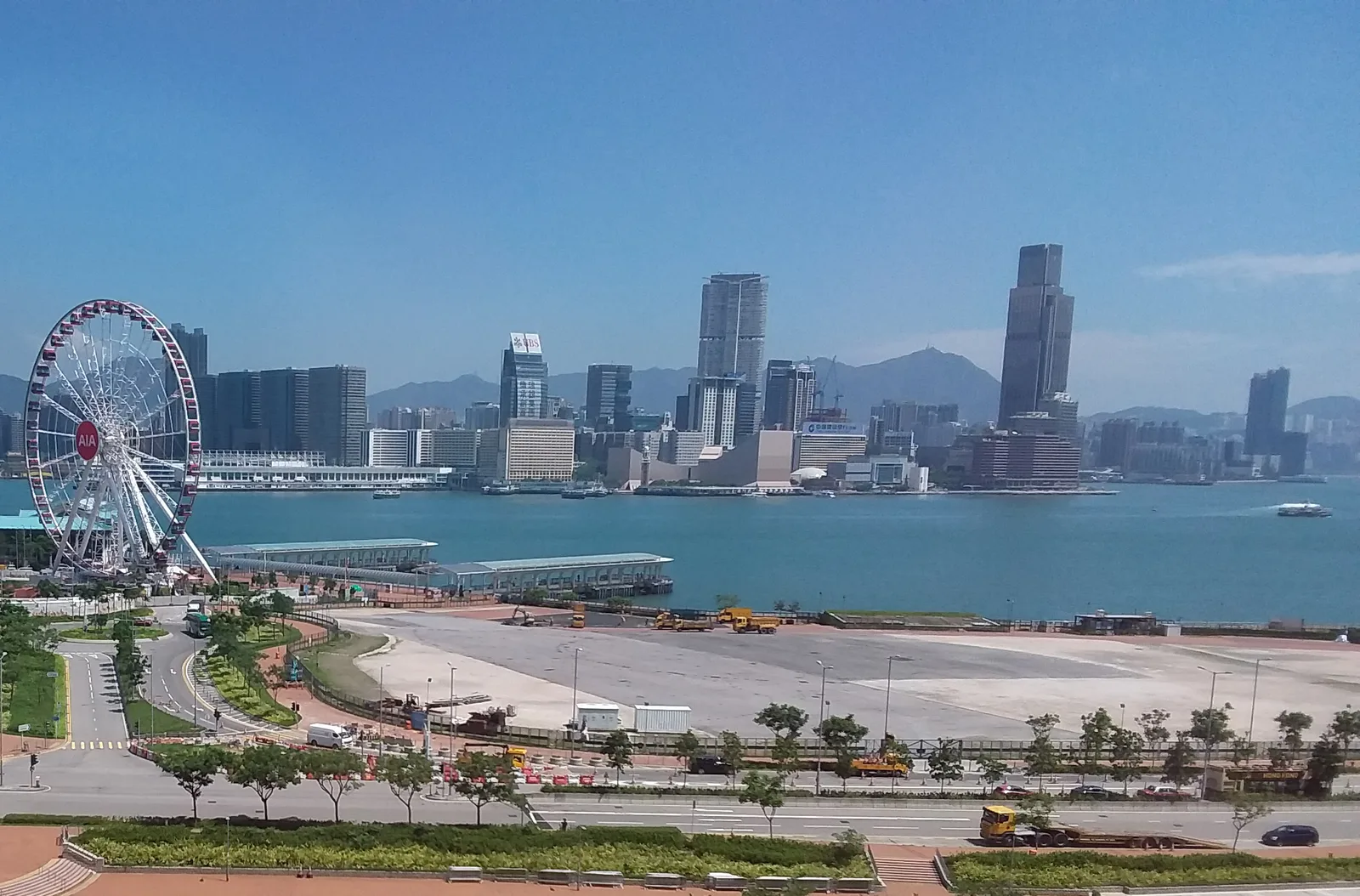 ลานกว้าง Central Harbourfront Event Space ริมอ่าวในย่านเซ็นทรัล ฮ่องกง มีชิงช้าสวรรค์และตึกสูงฝั่งเกาลูนเป็นฉากหลัง