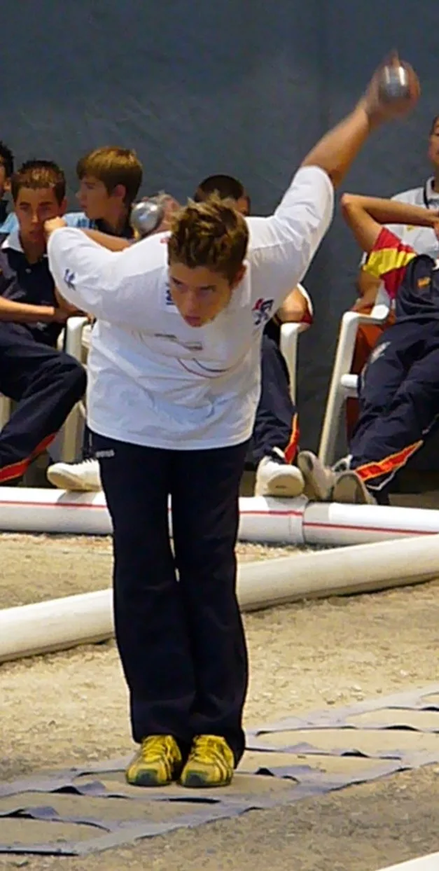 Dylan Rocher ในเสื้อขาว กางเกงกรมท่า เหวี่ยงแขนถือลูกเปตองเตรียมยิงตามกติกาเปตองยิงเป้า ในชิงแชมป์ยุโรปเยาวชนที่ Martigny ปี 2006