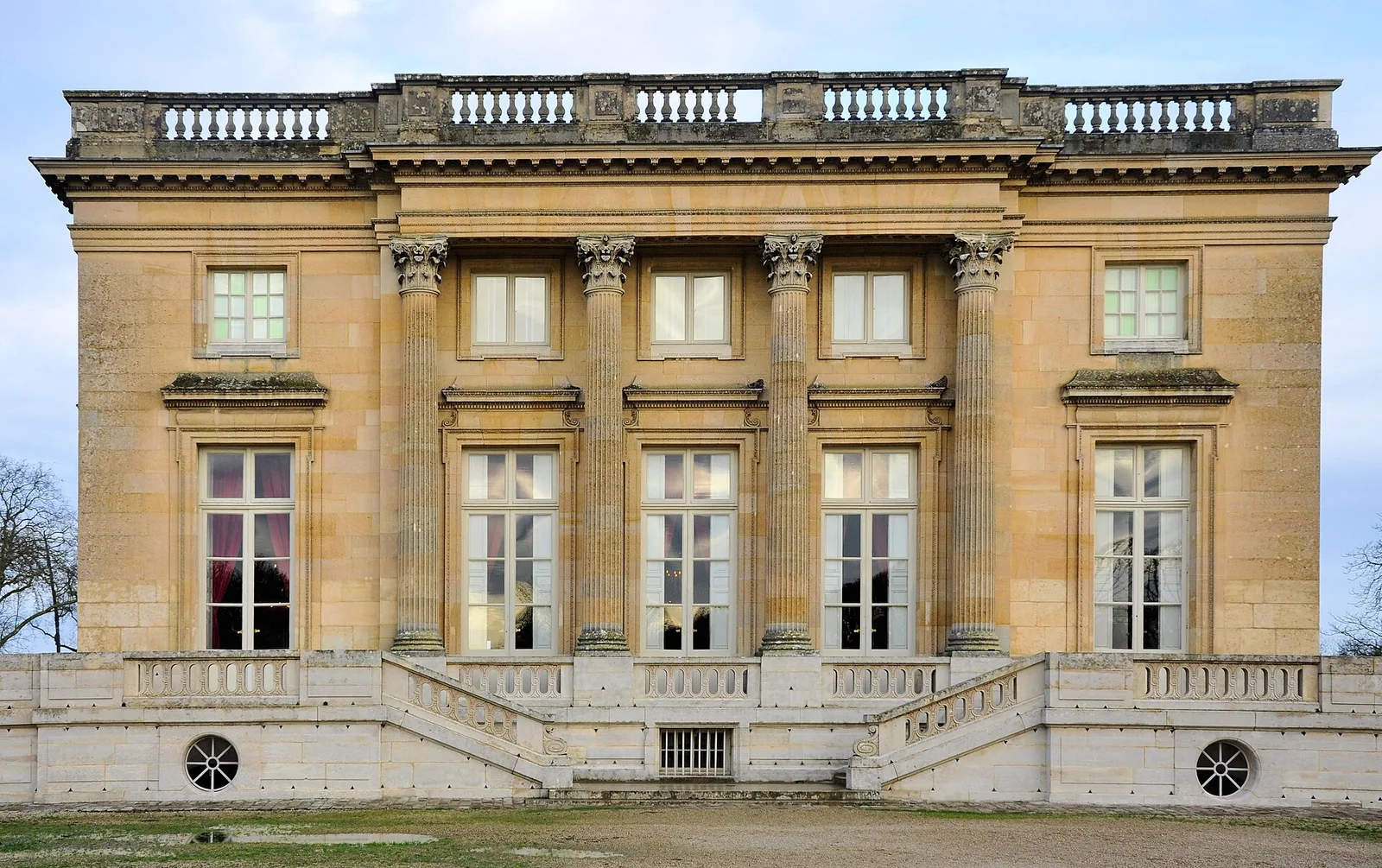 ด้านตะวันตกของ Petit Trianon อาคารหินทรงลูกบาศก์ เสาคอรินเทียนสี่ต้น และราวลูกกรงบนหลังคาแบน