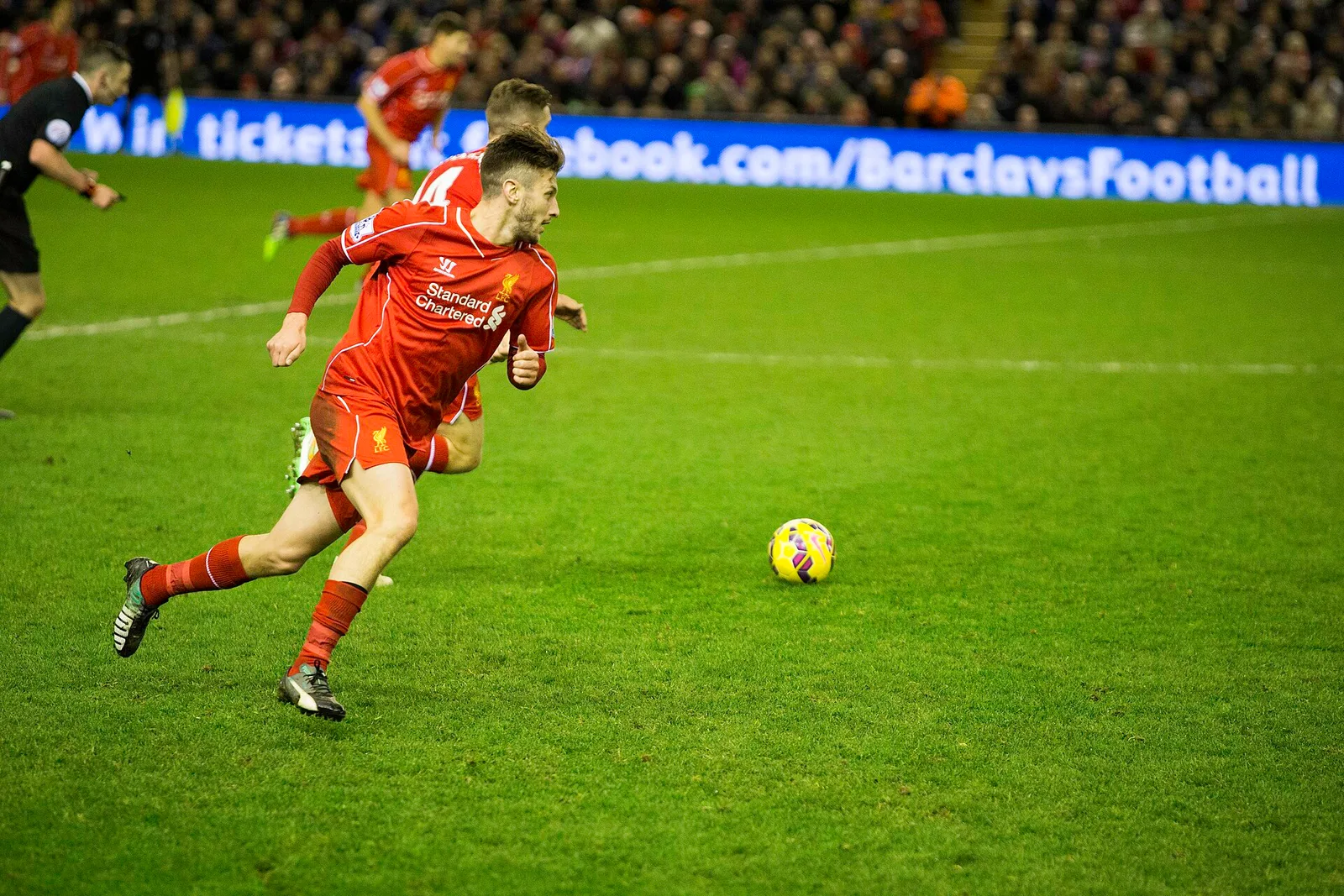 Adam Lallana ในชุดแข่งสีแดงของลิเวอร์พูล เลี้ยงบอลในเกมพรีเมียร์ลีกกับอาร์เซนอลที่ Anfield เมื่อ 21 ธันวาคม 2014
