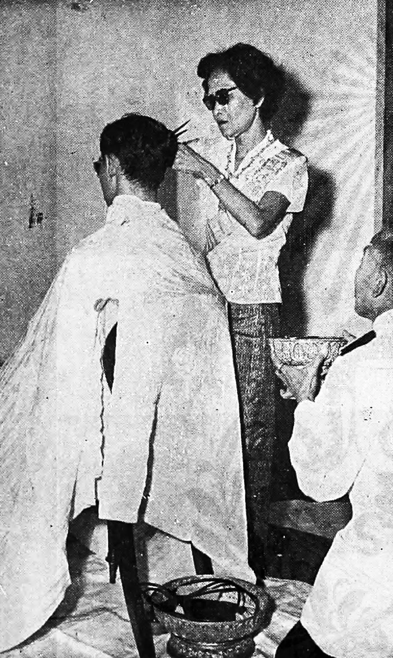 ภาพถ่ายเก่า พ.ศ. 2499 คำอธิบายในคลังภาพระบุว่า สมเด็จย่า เริ่มปลงพระเกศาให้รัชกาลที่ 9 ในพิธีผนวช ที่หลังพระอุโบสถวัดพระศรีรัตนศาสดาราม