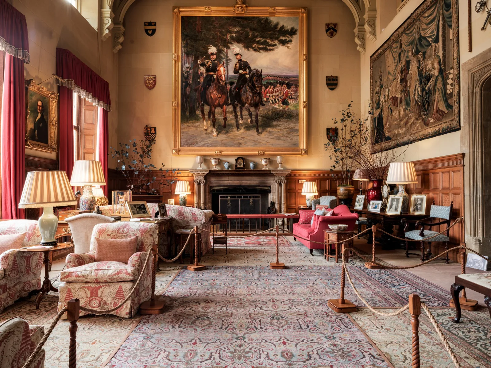 ห้องเพดานสูงภายใน Sandringham House แขวนภาพเขียนขนาดใหญ่เหนือเตาผิงและพรมทอผนัง มีเชือกกั้นเส้นทางผู้ชม