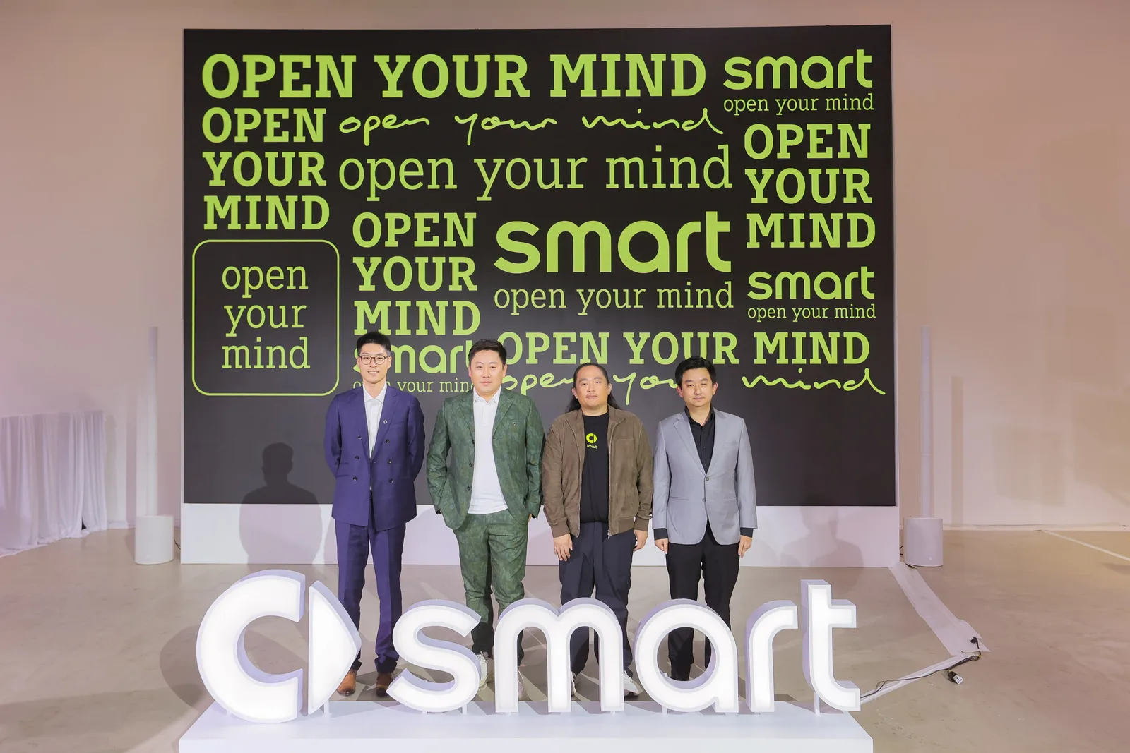 ผู้บริหารยืนบนเวทีงาน smart เปิดตัวในไทยร่วมกับ Thonburi Group หน้าฉากข้อความ open your mind และโลโก้ smart