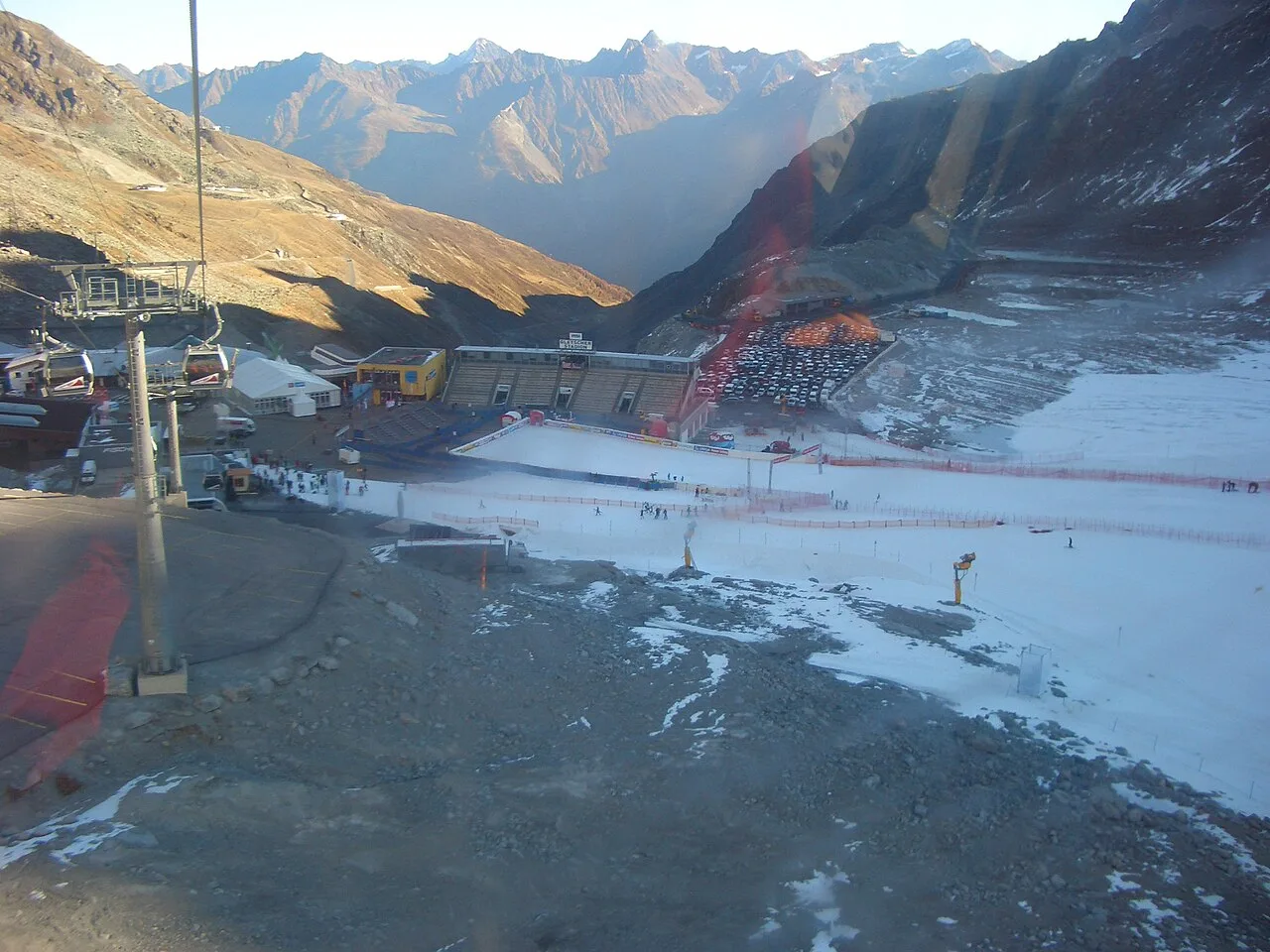 พื้นที่เส้นชัยและอัฒจันทร์ Gletscherstadion บนธารน้ำแข็ง Rettenbach ที่ Sölden มองจากกระเช้า เห็นลานจอดรถ เครื่องทำหิมะ และหุบเขาด้านล่าง ภาพวันที่ 24 ตุลาคม 2008