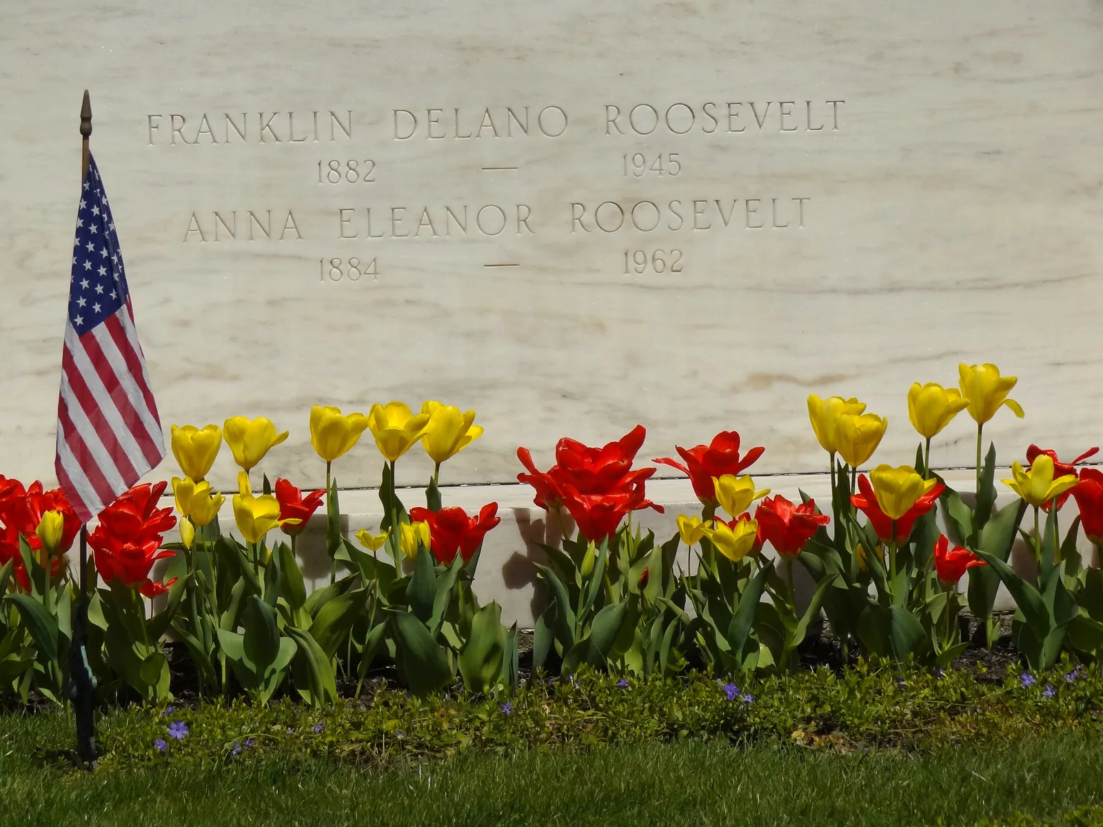 ป้ายหลุมศพสลักชื่อ Franklin Delano Roosevelt และ Anna Eleanor Roosevelt กับดอกทิวลิปและธงชาติสหรัฐฯ ภาพถ่ายเมื่อ 13 เมษายน 2012