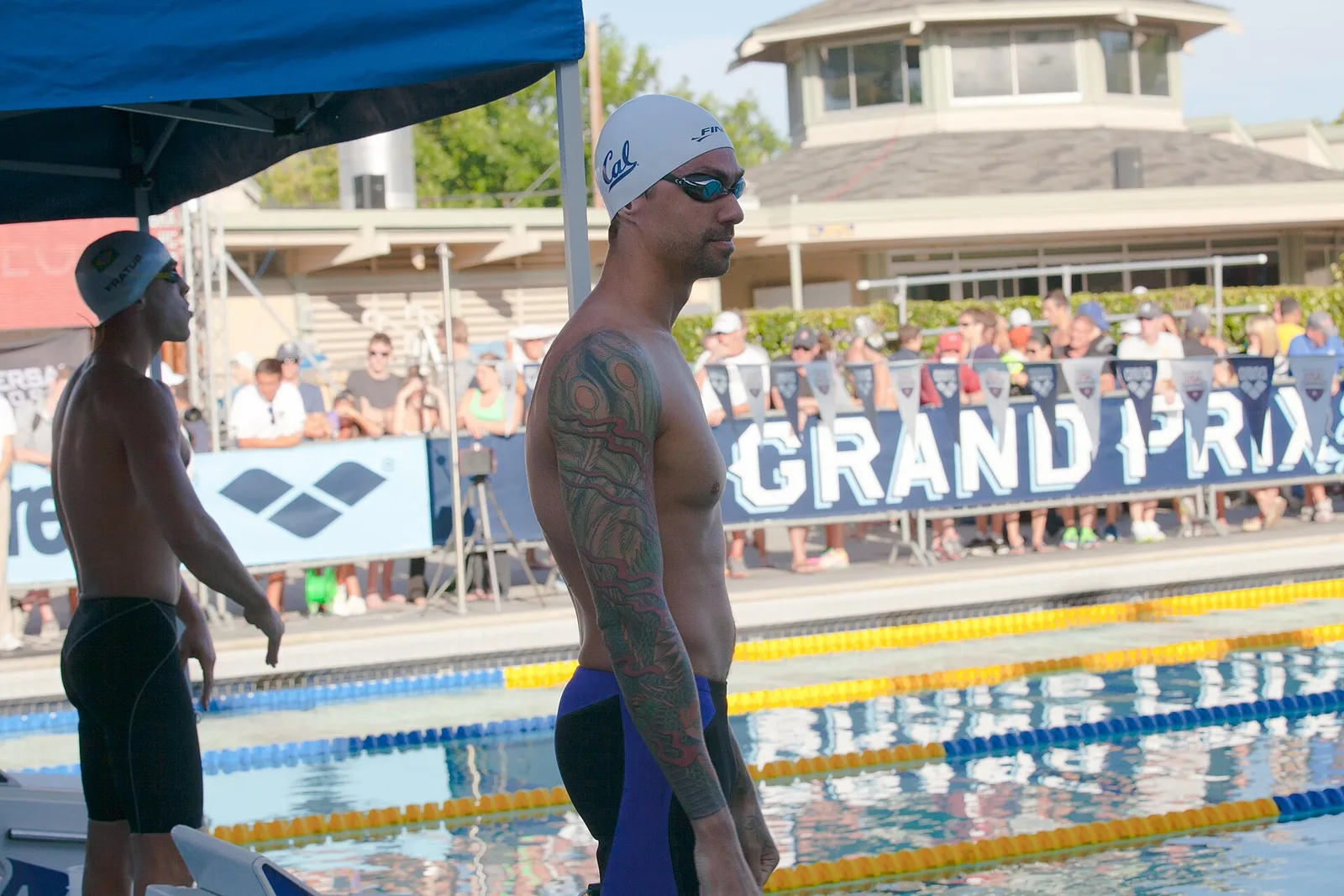 นักว่ายน้ำ Anthony Ervin สวมหมวกว่ายน้ำสีขาว แว่นตาว่ายน้ำ และกางเกงแข่งขันสีน้ำเงิน ยืนข้างสระที่มีทุ่นกั้นเลนก่อนแข่งฟรีสไตล์ 50 เมตร ปี 2014