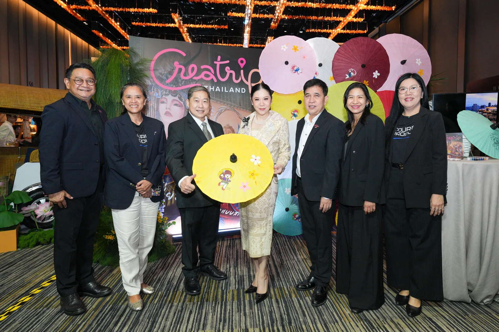กลุ่มผู้ร่วมงานยืนหน้าบูธ Creatrip Thailand ที่ตกแต่งด้วยร่มกระดาษสี ในงาน THAILAND NEXTPERIENCE ของ ททท.