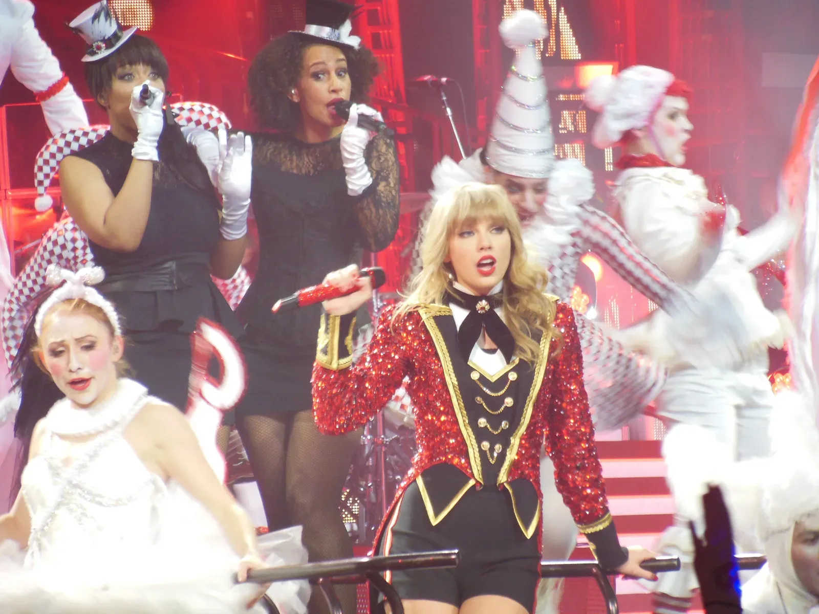 Taylor Swift ในแจ็กเก็ตเลื่อมสีแดงกลางนักเต้นบนเวที The Red Tour ปี 2013 ทัวร์ของอัลบั้ม Red ซึ่งเป็นบ้านแรกของ All Too Well