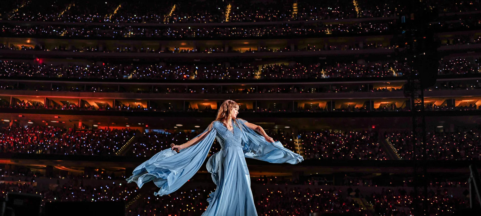 Taylor Swift ในชุดยาวสีฟ้าบนเวทีช่วง folklore ของ The Eras Tour ที่ SoFi Stadium เมือง Inglewood 9 สิงหาคม 2023 ท่ามกลางผู้ชมเต็มอัฒจันทร์