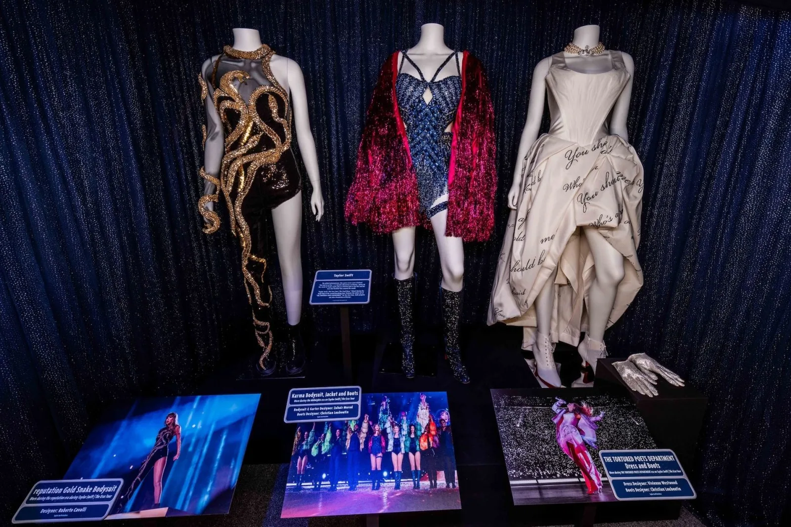 ชุดแสดง 3 ชุดของ Taylor Swift จาก The Eras Tour บนหุ่นในนิทรรศการที่ Walt Disney Presents ใน Disney's Hollywood Studios พร้อมป้ายระบุผู้ออกแบบและภาพบนเวที