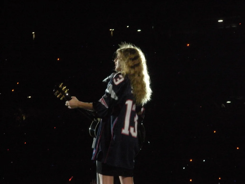 Taylor Swift ในเสื้อหมายเลข 13 หันหลังเล่นกีตาร์บนเวที Fearless Tour ที่ Foxboro รัฐ Massachusetts วันที่ 5 มิถุนายน 2010