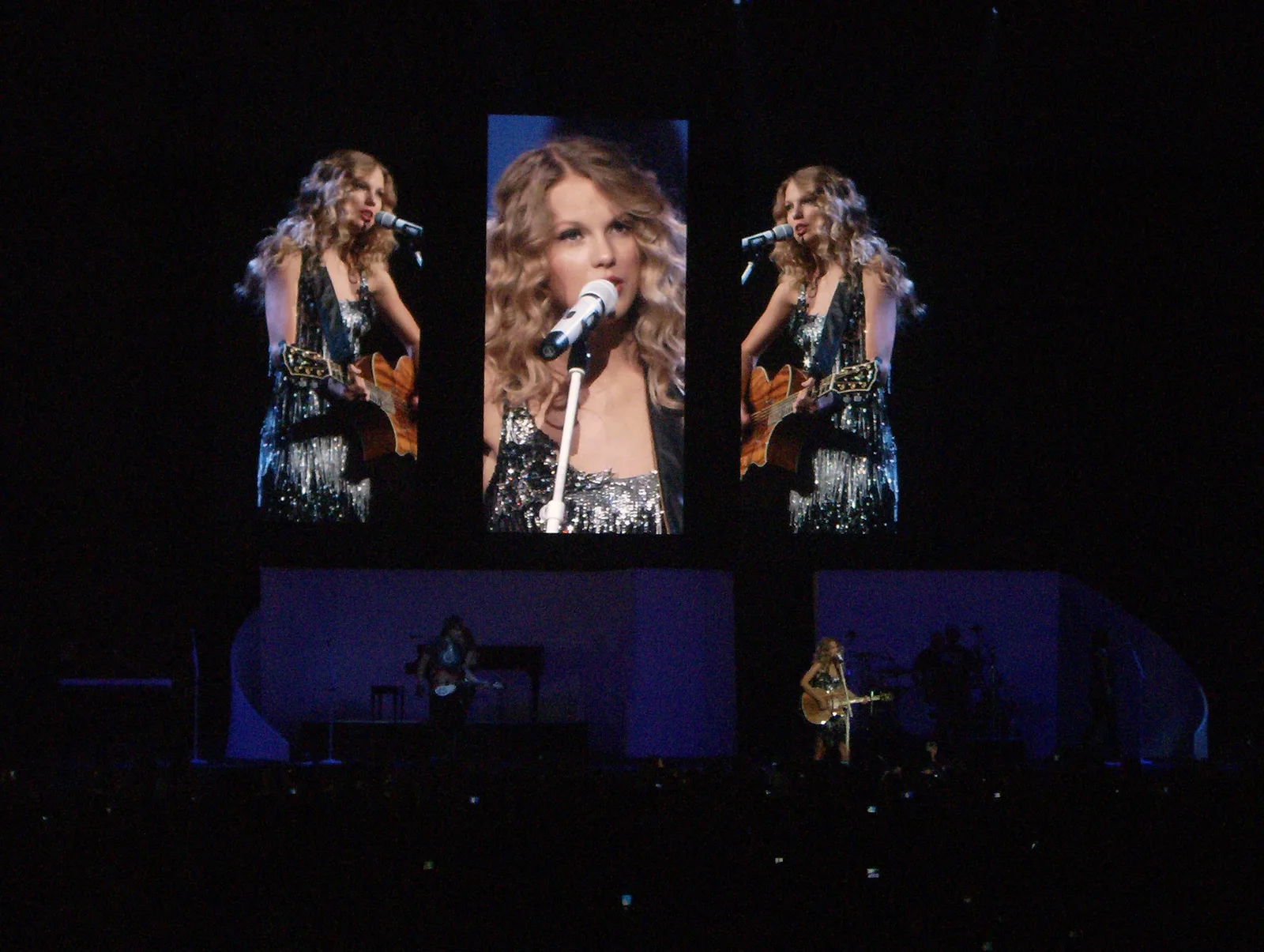 Taylor Swift บนเวที Fearless Tour ที่ Philadelphia รัฐเพนซิลเวเนีย วันที่ 1 สิงหาคม 2009 จอใหญ่สามจอฉายภาพเธอขณะร้องเพลง