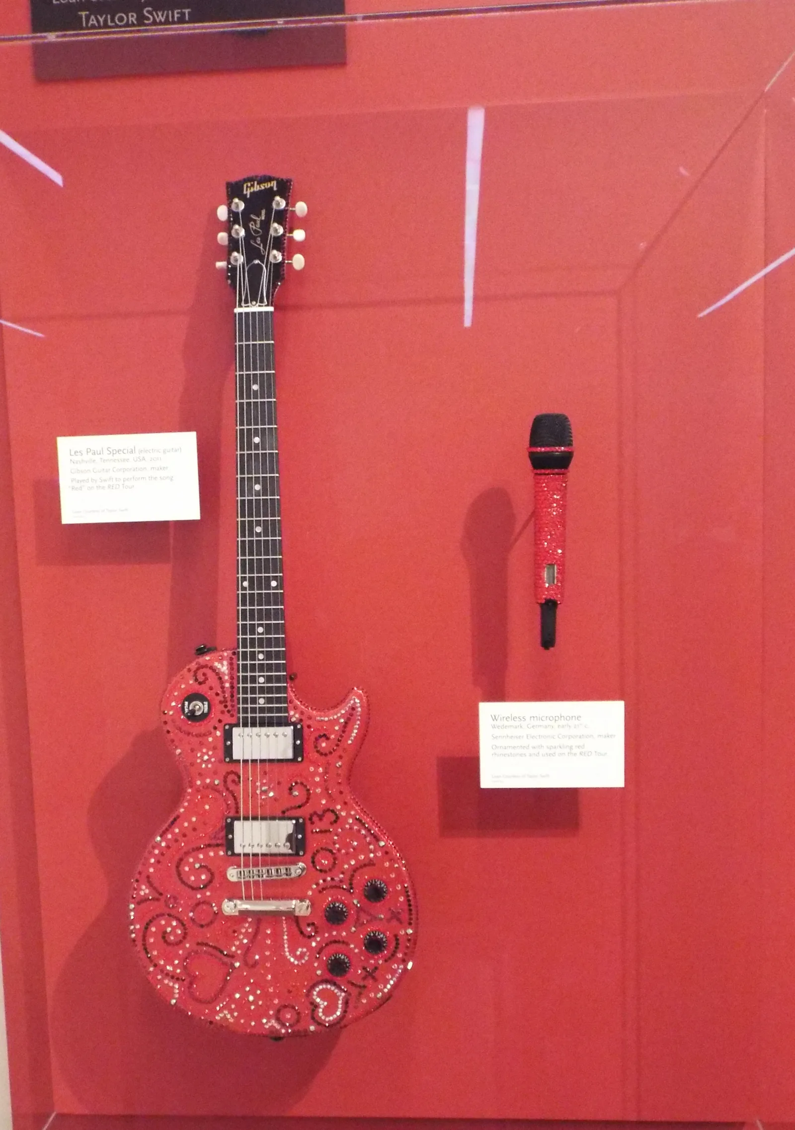 กีตาร์ Les Paul ลายสีแดงและไมโครโฟนไร้สายของ Taylor Swift ในตู้จัดแสดงของ Musical Instrument Museum เมือง Phoenix เดือนกุมภาพันธ์ 2017