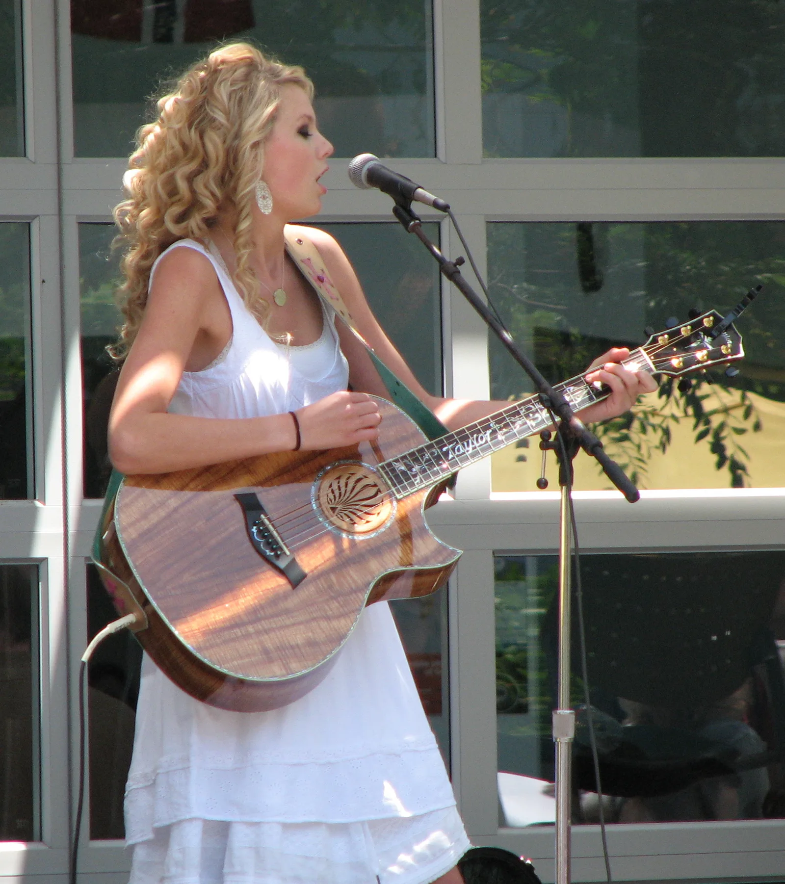 Taylor Swift ในชุดเดรสสีขาวร้องเพลงพร้อมกีตาร์โปร่งหน้าไมโครโฟน ขณะแสดงที่ Yahoo เดือนพฤษภาคม 2007