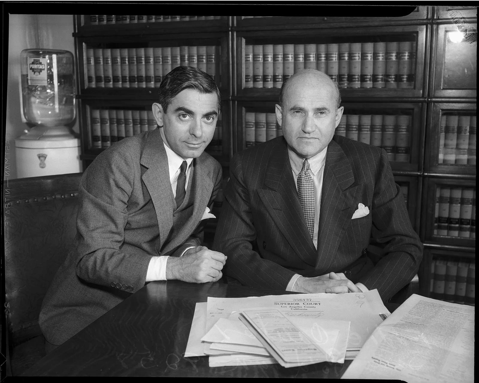 Eddie Cantor (ซ้าย) และ Samuel Goldwyn (ขวา) นั่งที่โต๊ะหน้าตู้หนังสือ ภาพราวปี 1934 จาก Los Angeles Daily News
