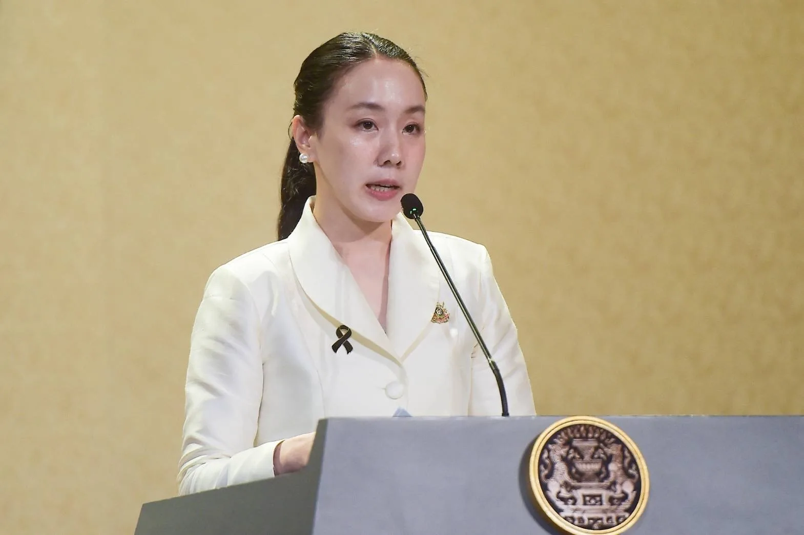 รองโฆษกประจำสำนักนายกรัฐมนตรียืนแถลงหลังโพเดียมที่มีตราสัญลักษณ์รัฐบาล ภาพประกอบประกาศยอดใช้จ่ายไทยช่วยไทย พลัส 60/40 เพิ่มเติม วันที่ 18 ตุลาคม 2569