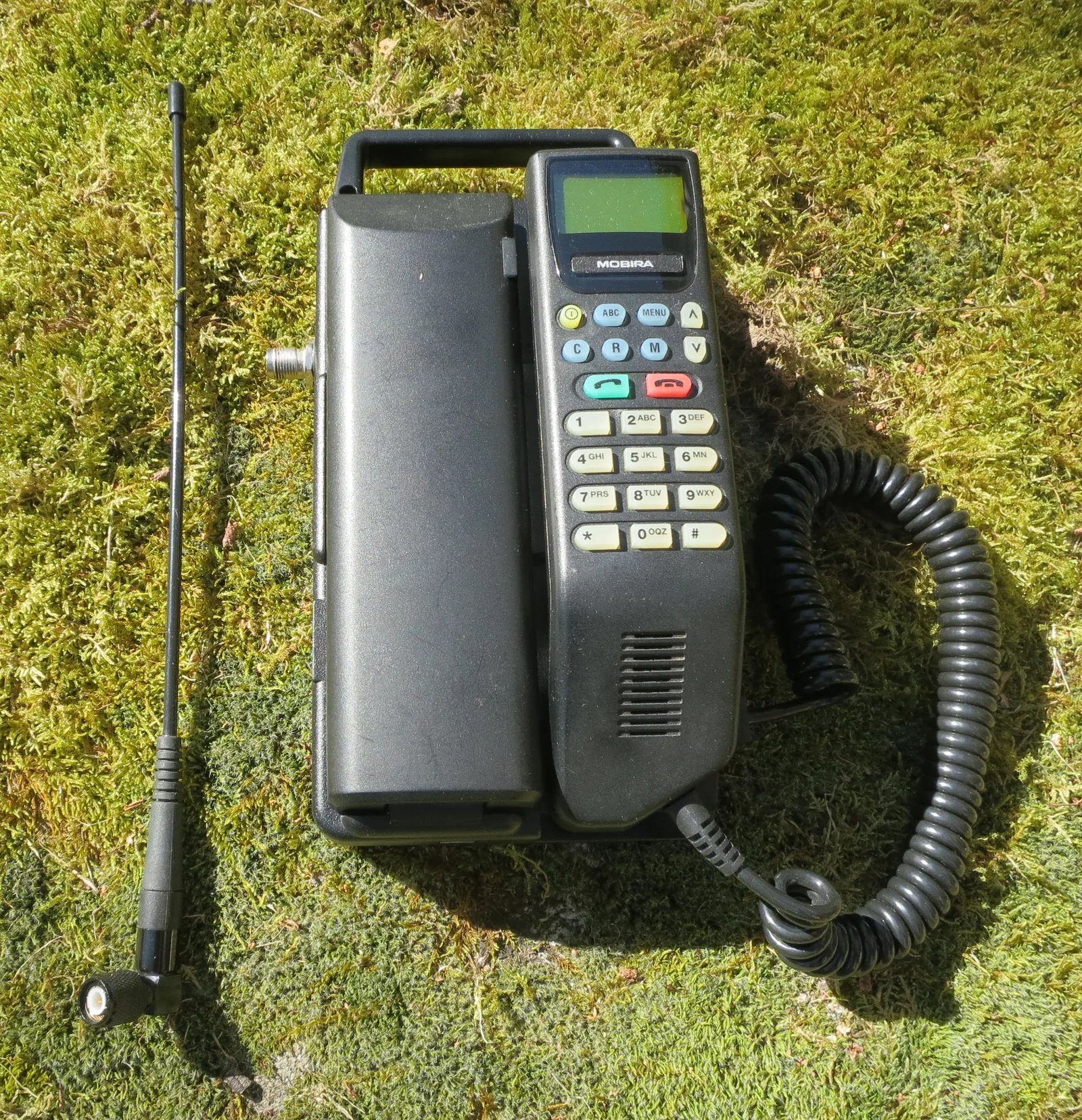 โทรศัพท์ระบบ NMT 450 ของ Nokia-Mobira รุ่น TMF-4SP ผลิตในฟินแลนด์ ค.ศ. 1994 ตัวเครื่องมีหูโทรศัพท์ แป้นกด สายขด และเสาอากาศแยก วางบนพื้นหญ้า