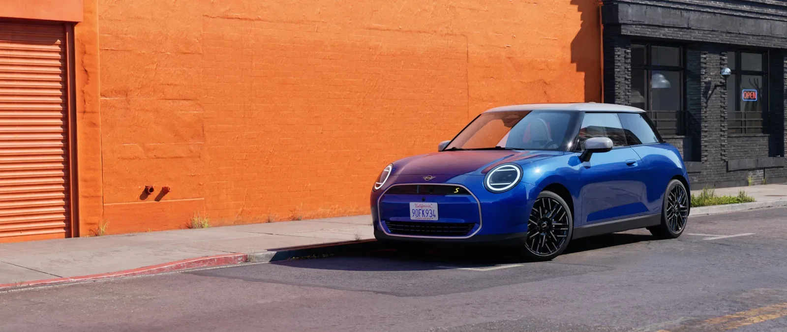 MINI Cooper SE ไฟฟ้าสีน้ำเงินหลังคาขาว จอดริมถนนหน้ากำแพงสีส้ม ภาพจากหน้ารุ่น Cooper ไฟฟ้าของ MINI ประเทศไทย