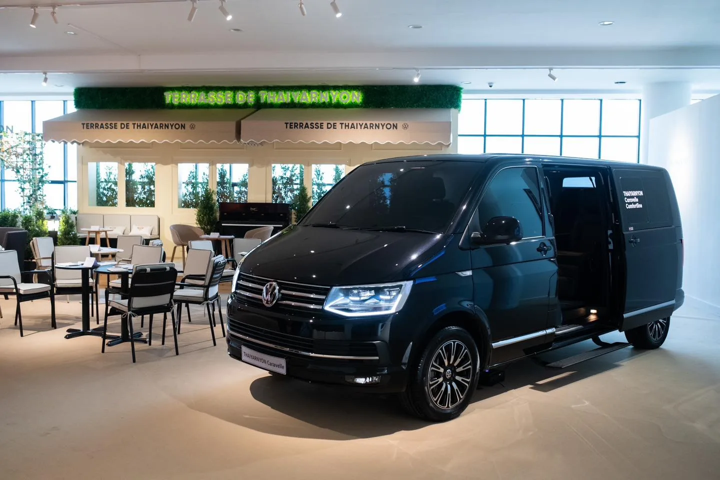 Volkswagen Thaiyarnyon Caravelle Comfortline NGZ สีดำ เปิดประตูสไลด์ข้าง จอดในโชว์รูมพระราม 9 ที่มีป้าย Terrasse de Thaiyarnyon