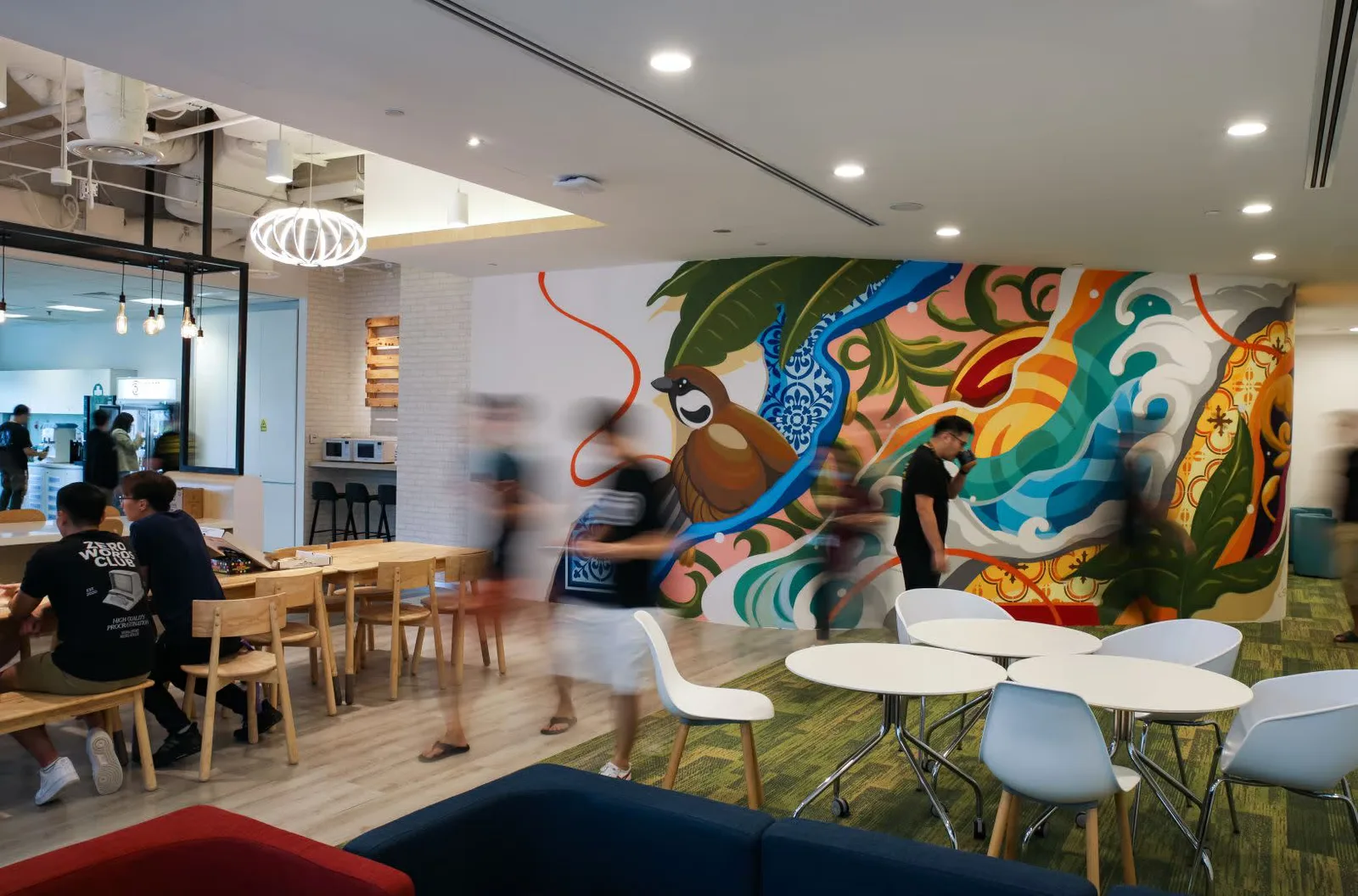 พื้นที่ส่วนกลางภายในสตูดิโอ Ubisoft Singapore ที่มีภาพจิตรกรรมฝาผนังและโต๊ะสำหรับพนักงาน