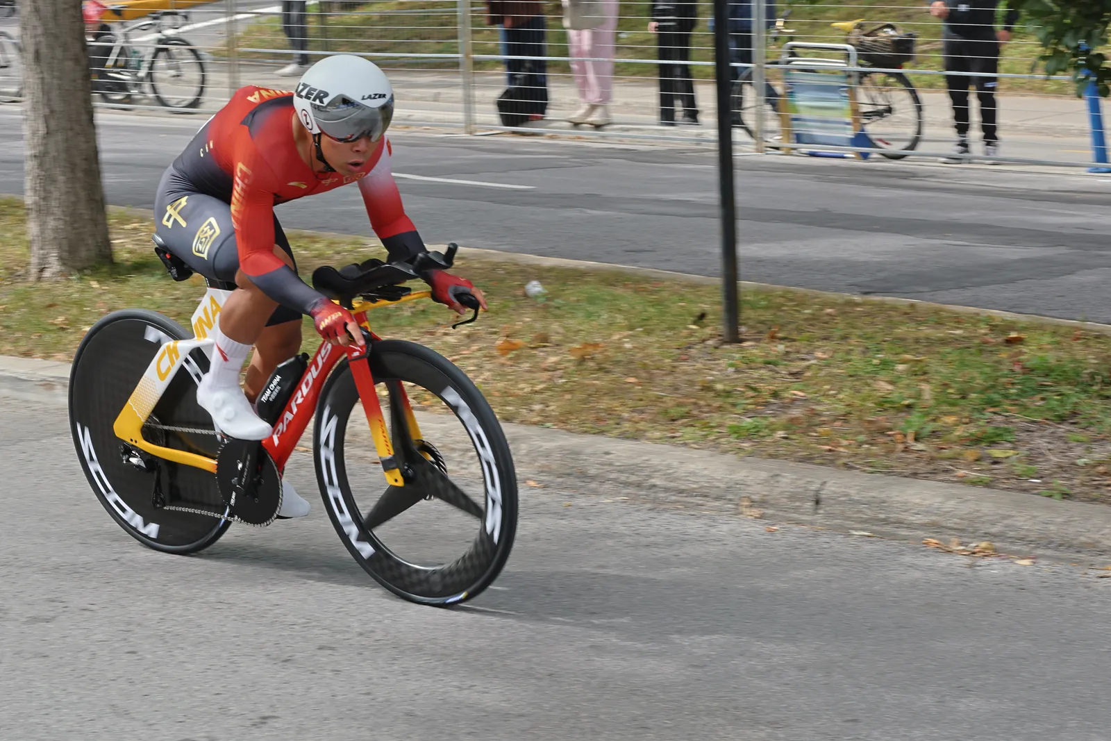Liu Chenglu นักปั่นจีน ในชุด skinsuit สีแดงเหลือง หมวกจับเวลาสีขาว บนจักรยานจับเวลาสีแดงเหลืองพร้อมแอโรบาร์ ล้อหน้าขอบสูงและล้อหลังแบบดิสก์ ระหว่างแข่งจับเวลาชายในชิงแชมป์โลกจักรยานถนนของ UCI ที่ Montréal 20 กันยายน 2026