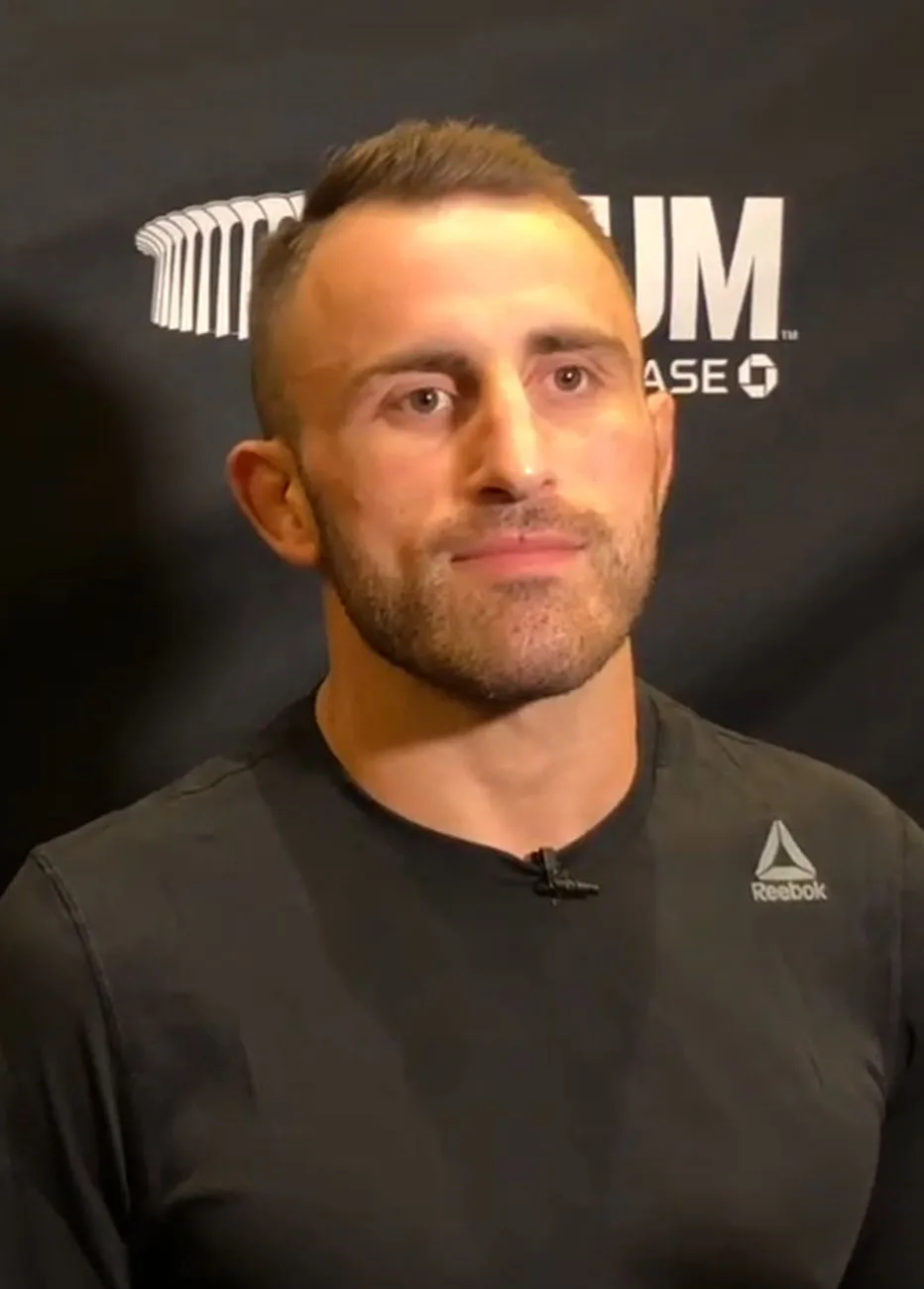 Alexander Volkanovski สวมเสื้อยืดสีดำให้สัมภาษณ์หน้าฉากโลโก้ในรายการ UFC 232 ปี 2018