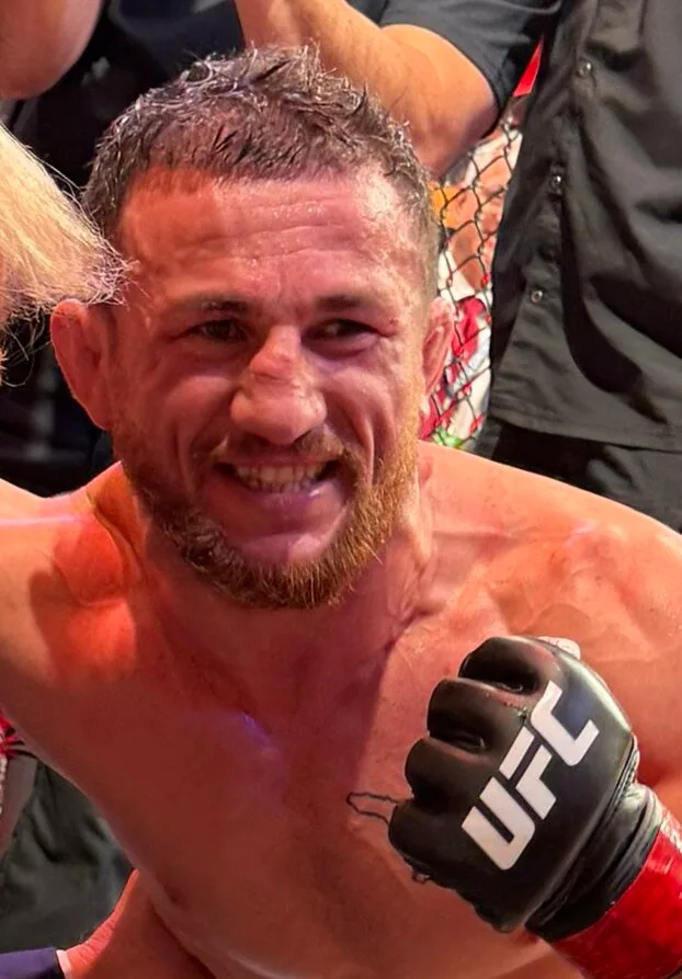 Merab Dvalishvili สวมถุงมือ MMA ของ UFC ยิ้มข้างกรงในคืนรายการ UFC 316 ปี 2025