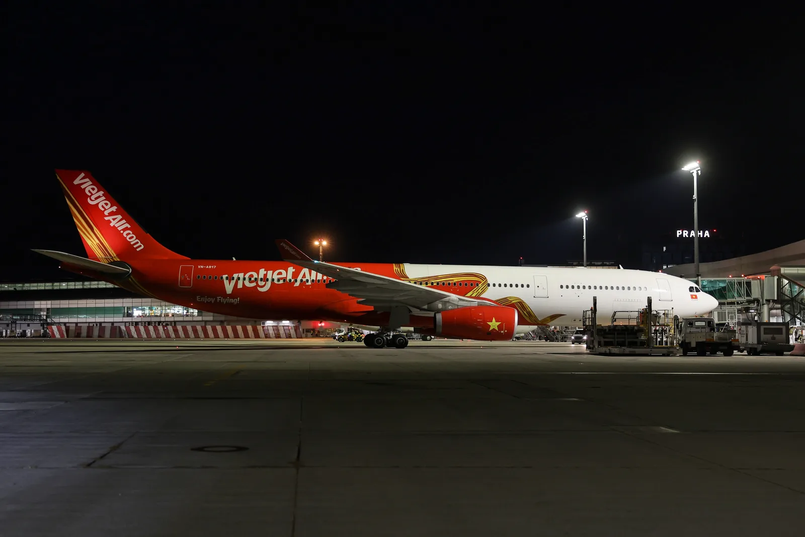 เครื่องบิน Airbus A330 ของ Vietjet จอดที่ท่าอากาศยานปรากตอนกลางคืน มีป้าย PRAHA บนอาคารผู้โดยสาร